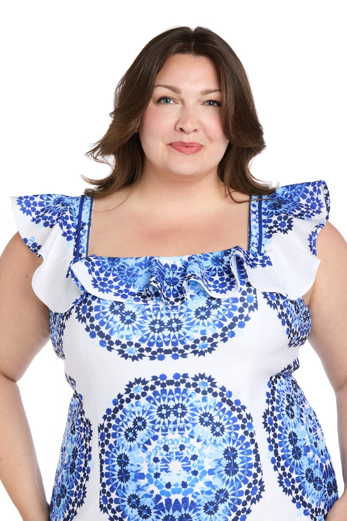 A woman with medium-length brown hair wears the R&M Richards 4134W plus-size short party dress, featuring a blue print and ruffled sleeves, while standing against a white background.