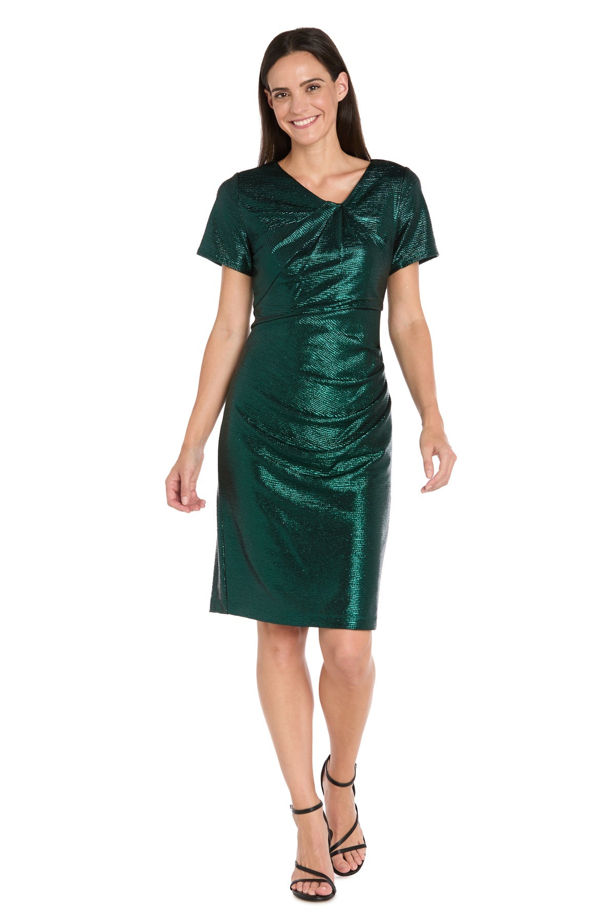 A woman stands smiling in the R&M Richards 4177, a short sleeve metallic green cocktail dress with a subtle shimmer. The knee-length party dress is paired with black strappy heels for a chic look.