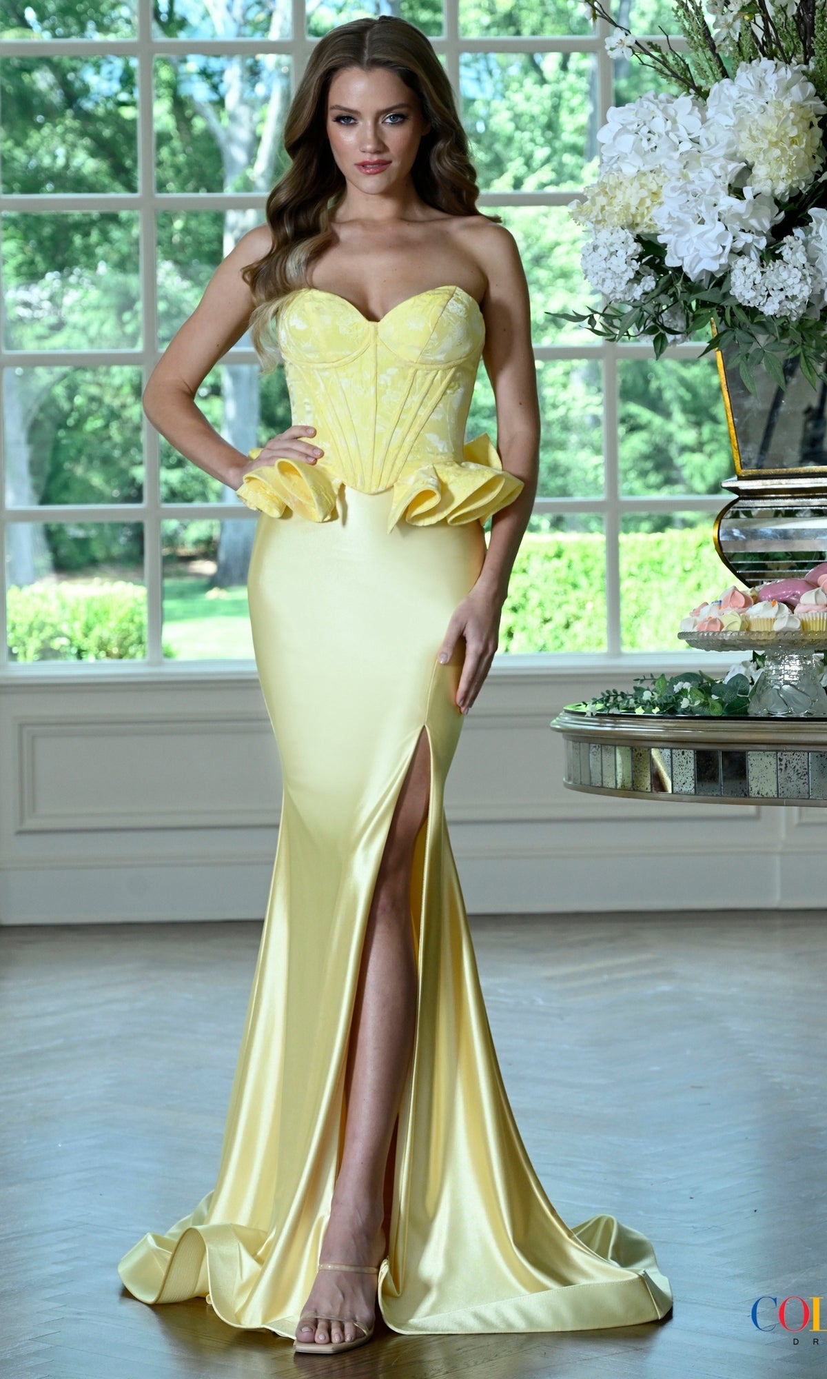 A yellow strapless floor-length Colors Dress 4181 prom dress with a peplum waist and a thigh-high slit.