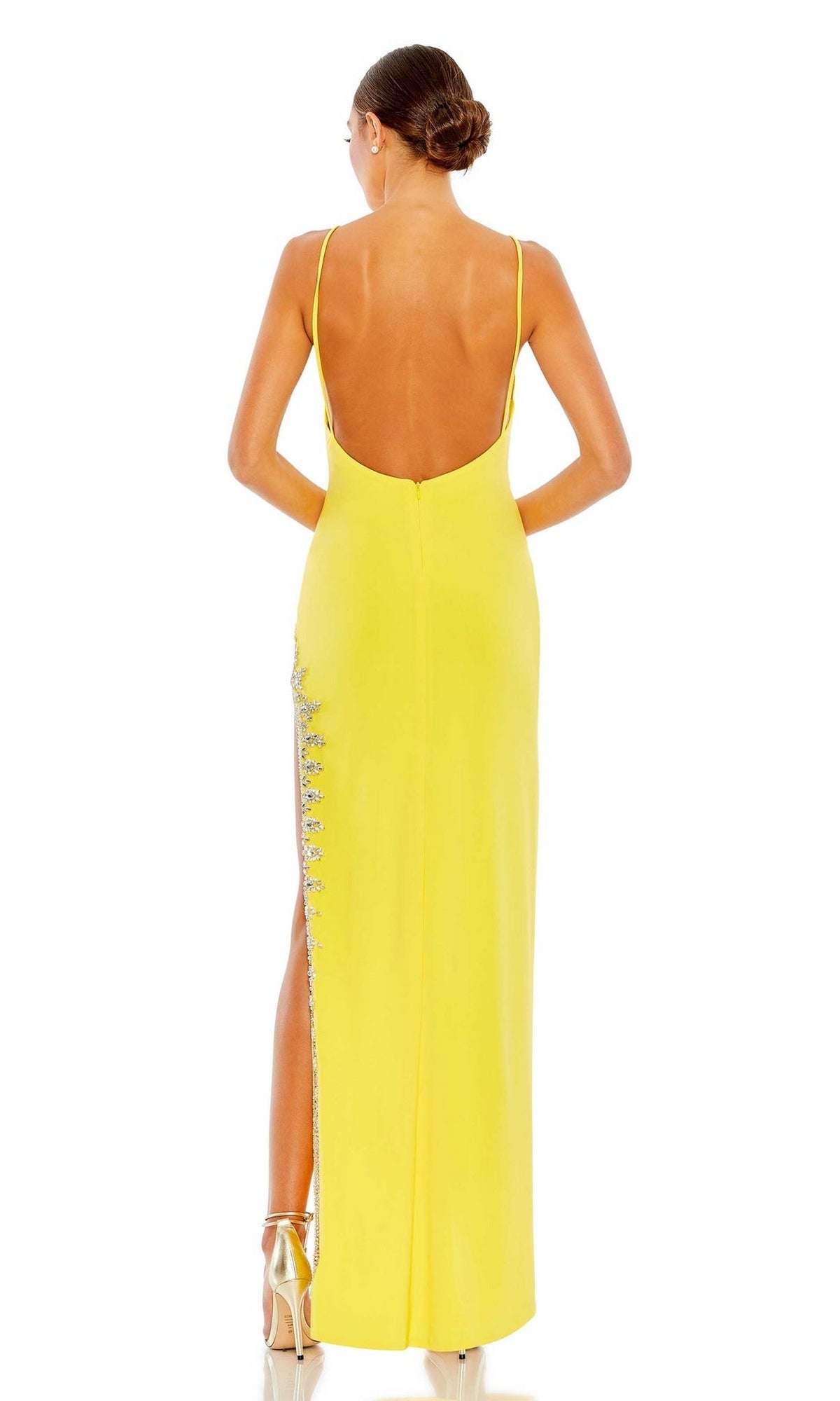 A woman stands facing away in the Mac Duggal 42002 bead-trimmed yellow formal dress, featuring thin straps, an open back, side embellishments, and high heels.