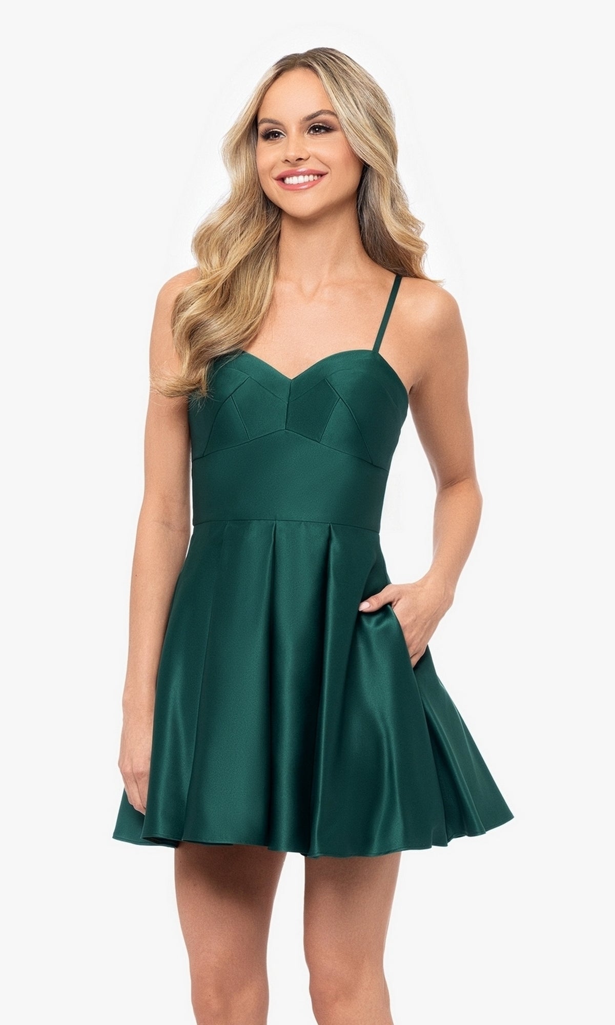 A woman stands and smiles against a plain white background, wearing the Short Satin A-Line Homecoming Dress 4200BN in emerald green with thin straps, a fitted bodice, and a sleeveless design.