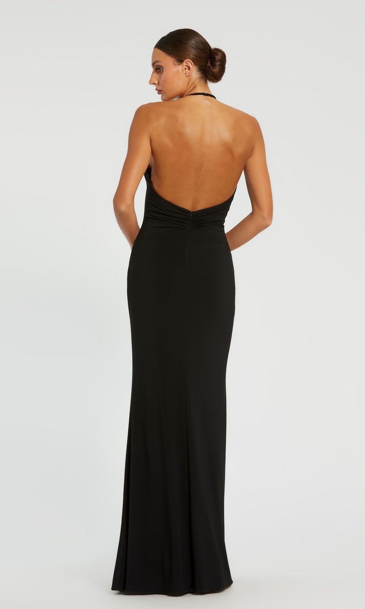 Woman in a Backless High-Neck Long Black Formal Dress 42065, standing with her hands behind her, facing away from the camera against a plain background.