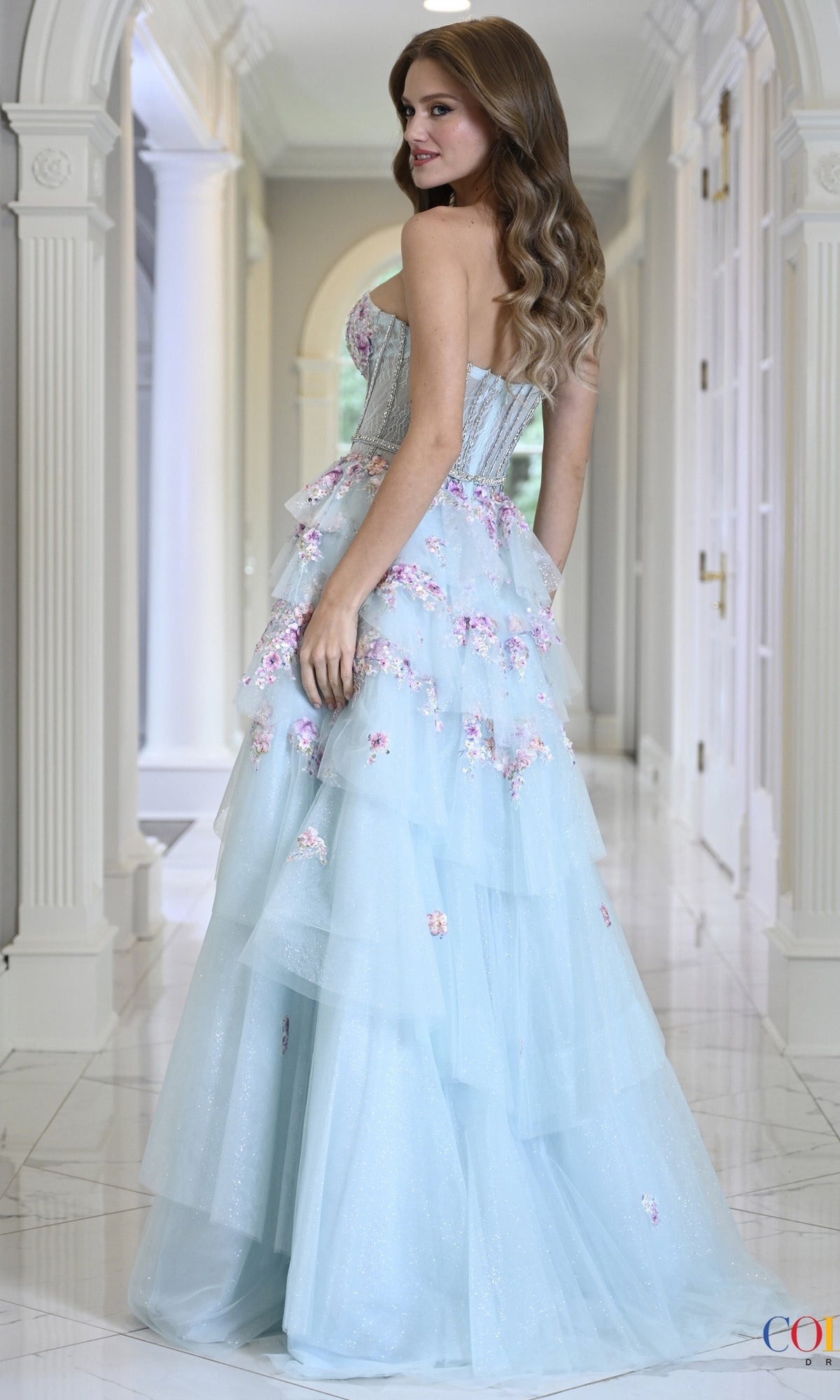 Colors Dress 4209 is a strapless, light blue floor-length floral glitter tulle prom dress with a corset-style bodice and a tiered skirt embellished with 3D flower embroidery.