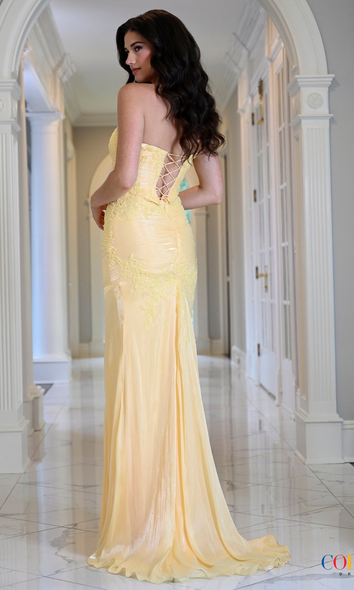 A woman wearing a Long Prom Dress: Colors Dress 4213, a draped, fitted, strapless floor-length yellow gown with a lace-up back design.