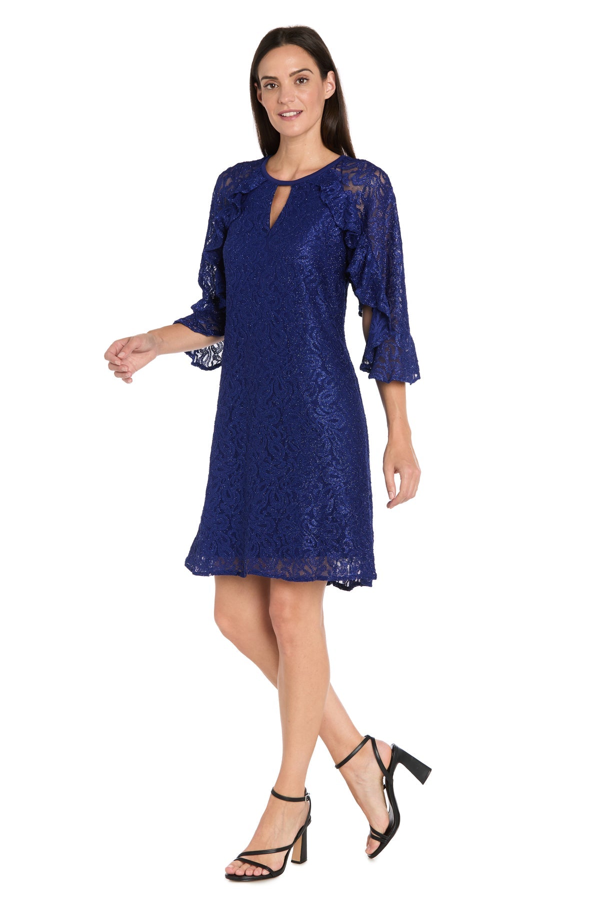 A woman models the R&M Richards 4226 Short Lace Semi-Formal Dress, featuring royal blue glitter lace, knee-length cut, and three-quarter bell sleeves with black heeled sandals against a white background.