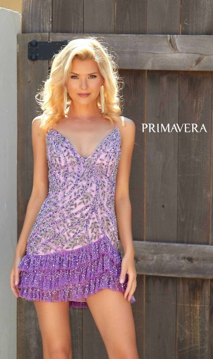 A woman wears the Short Homecoming Dress 4242 by Primavera—a sparkly, purple ruffle-layered dress with a lace-up back—standing before a wooden gate with