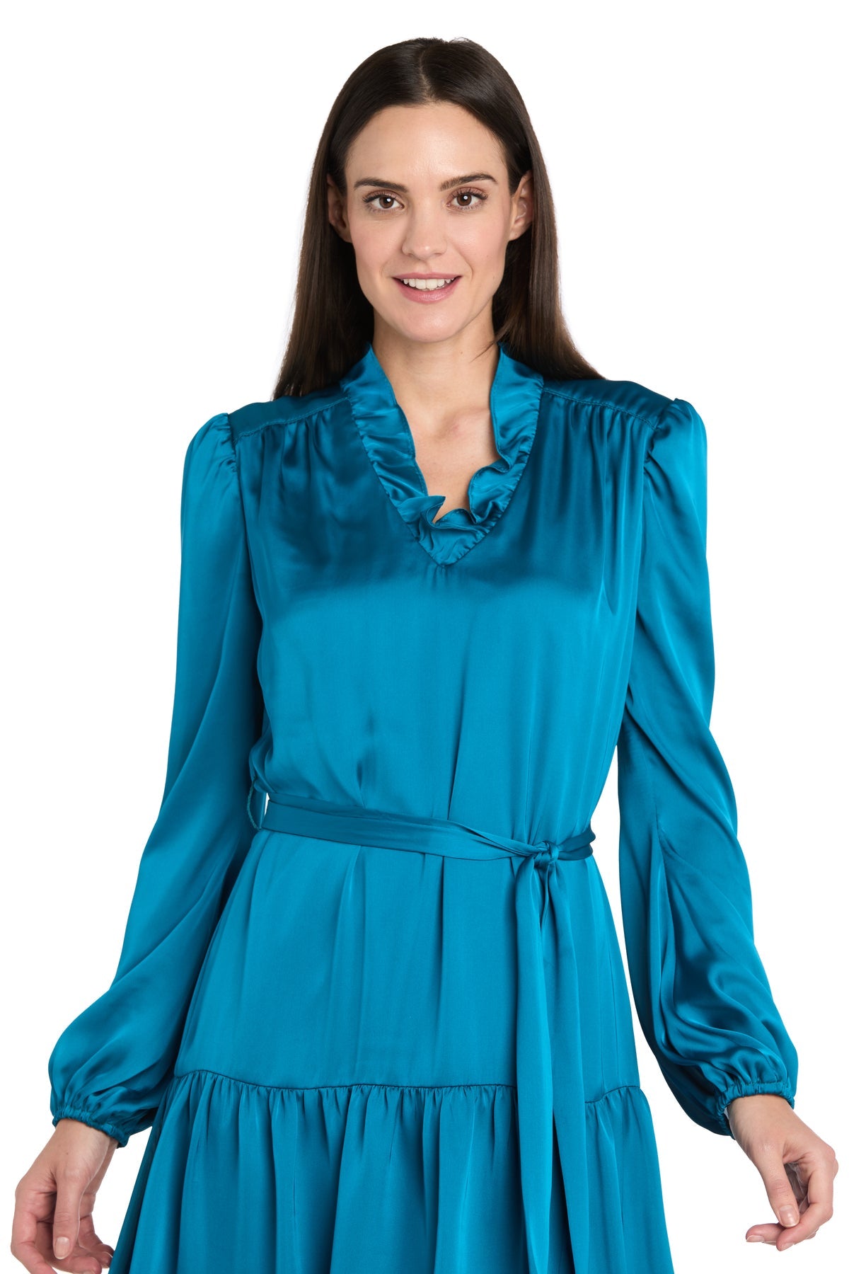 Woman in the R&M Richards 4246P Petite Short Teal Party Dressโan elegant knee-length dress with long sleeves, belted waist, and ruffled necklineโstands smiling at the camera.