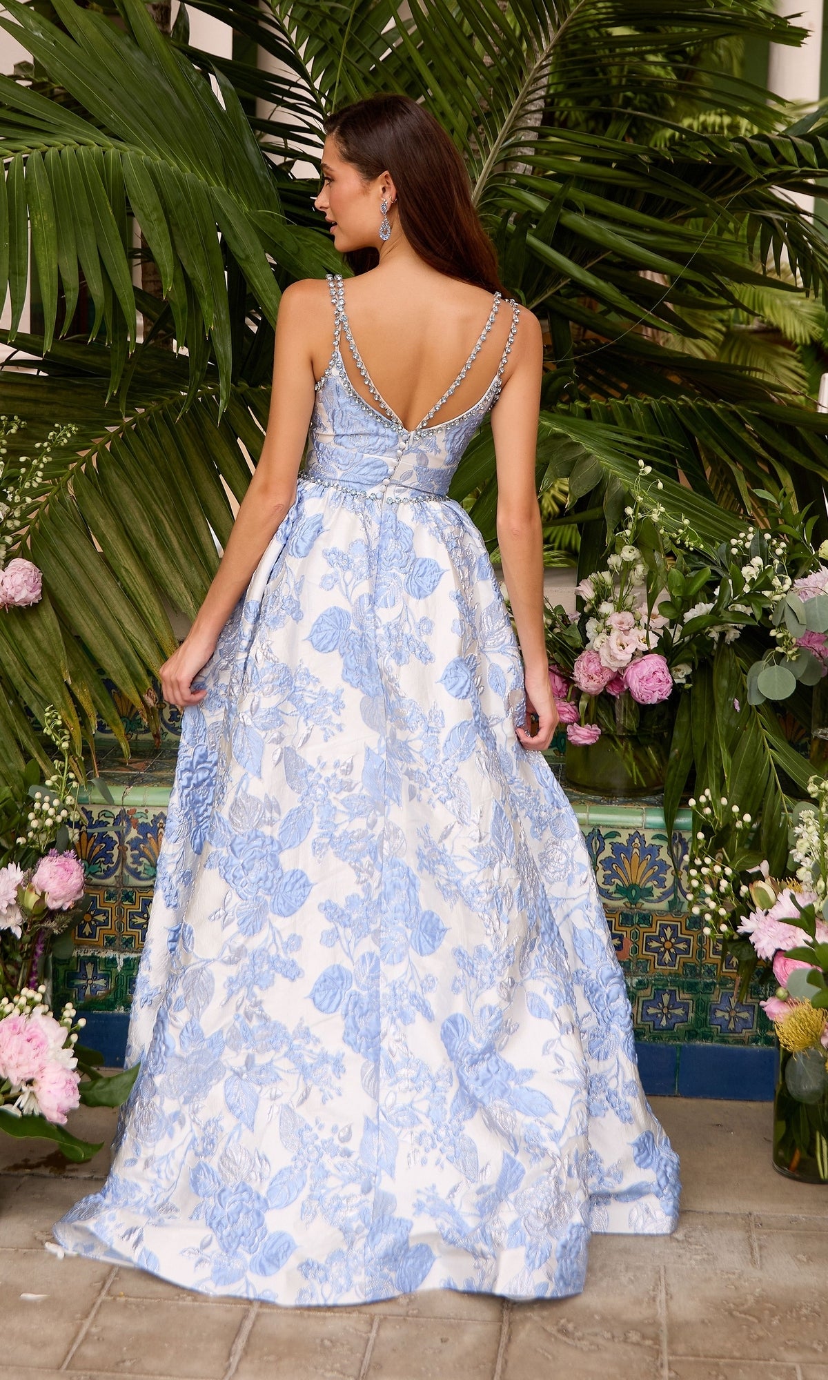 Back view of the Long Prom Dress: Ava Presley 42549, featuring a sleeveless, floor-length A-line silhouette with a blue and white floral print and a beaded crossover back strap.
