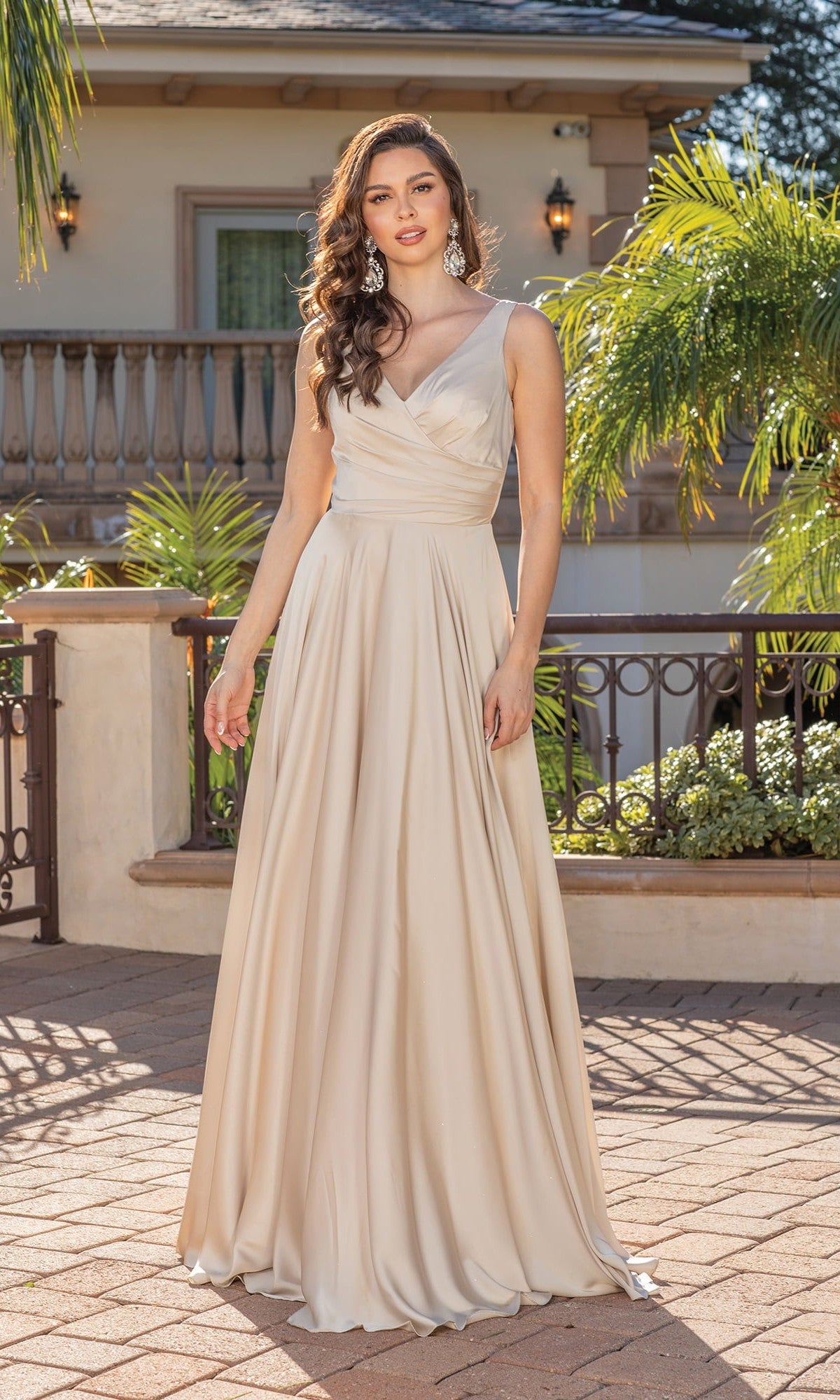 A woman stands outdoors in front of a building, wearing the Wrap-Bodice Long A-Line Prom Dress 4262—a sophisticated, champagne-colored satin gown featuring a V-neck and gathered waist.