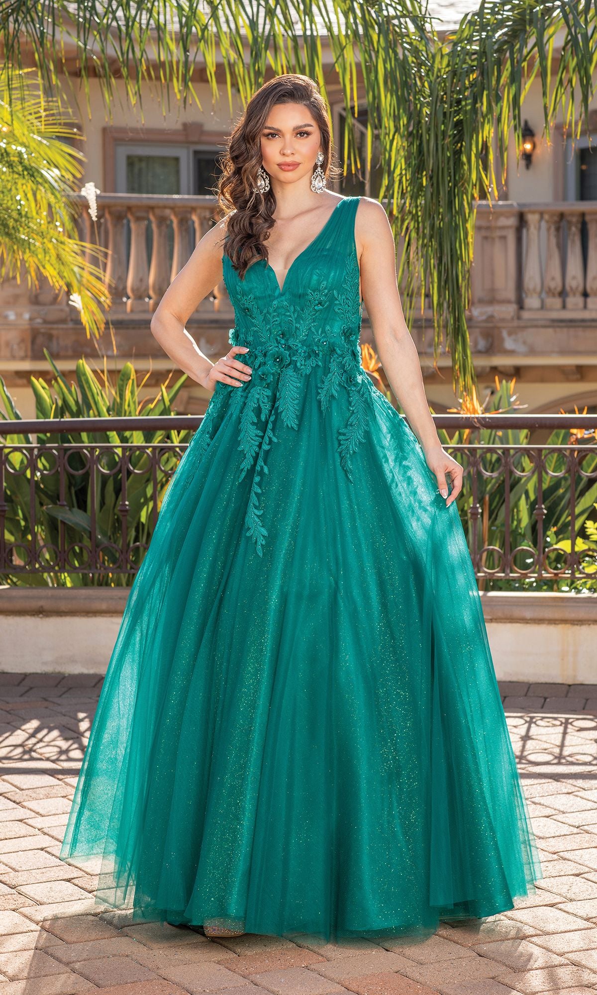 A woman stands outdoors in the Backless Glitter Tulle Ball Gown Prom Dress 4272, a floor-length sleeveless gown with a full tulle skirt, posing before a balcony and palm trees.