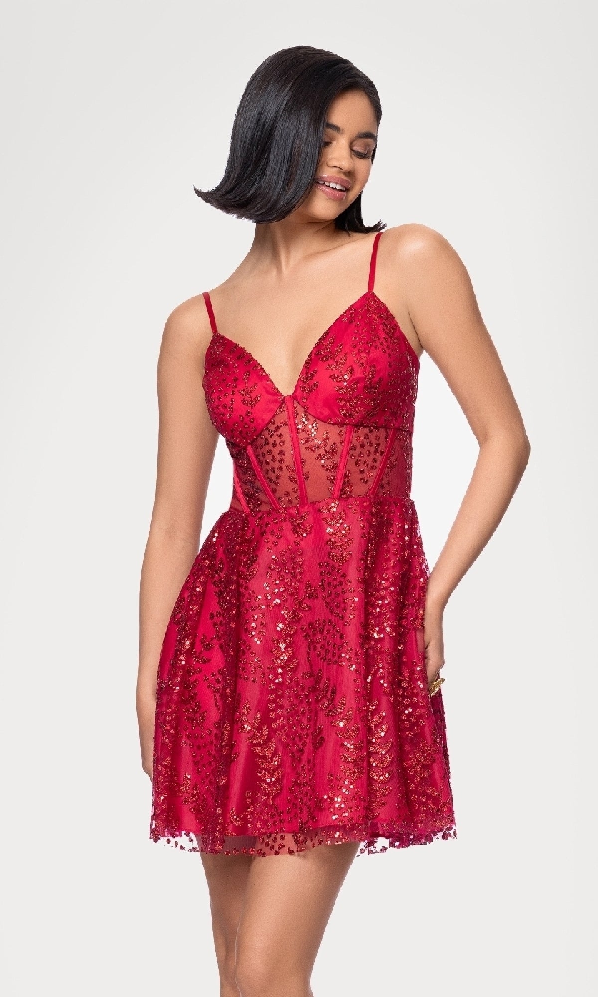 A woman stands against a white background, smiling to the side in the Blondie Nites 4279BN Short Red Glitter Hoco Dress featuring sequins and a sheer midsection.