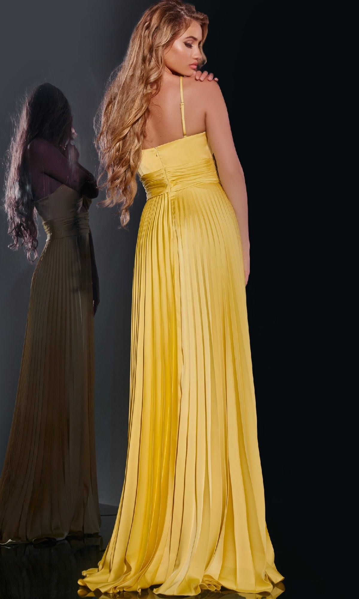 A woman wearing the Jovani 42971 long prom dress with pleated a-line skirt and adjustable spaghetti straps stands with her back to the camera, her reflection visible in a nearby mirror.