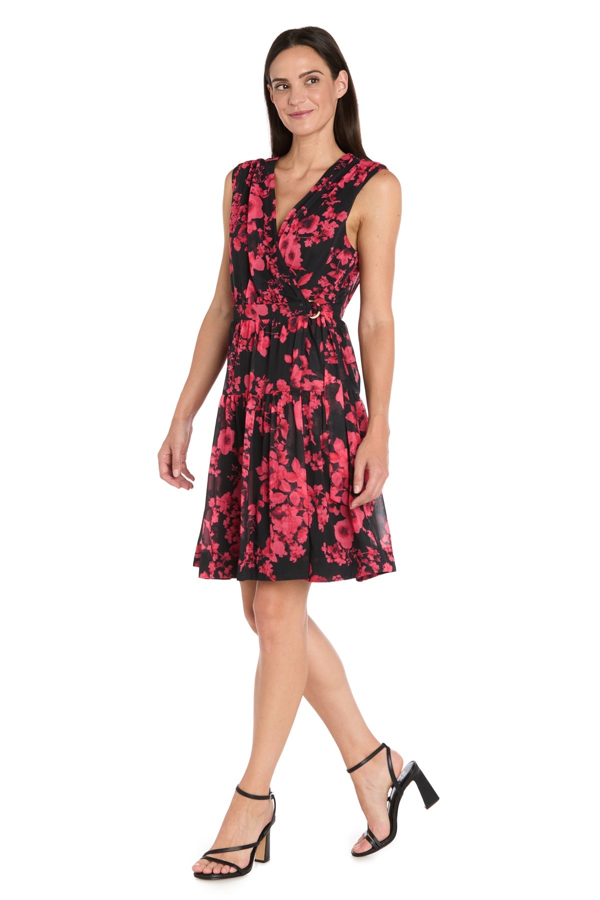 Woman modeling the R&M Richards 4299 Red Print Wedding Guest Dress, a sleeveless, knee-length black cocktail dress with red floral pattern, paired with black heeled sandals against a white backdrop.