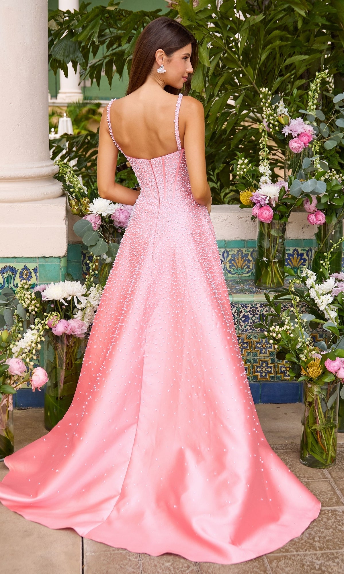 A woman wearing the Long Prom Dress: Ava Presley 43065, a floor-length, pink, pearl-adorned gown with a square neckline, thin straps, and a corset bodice.