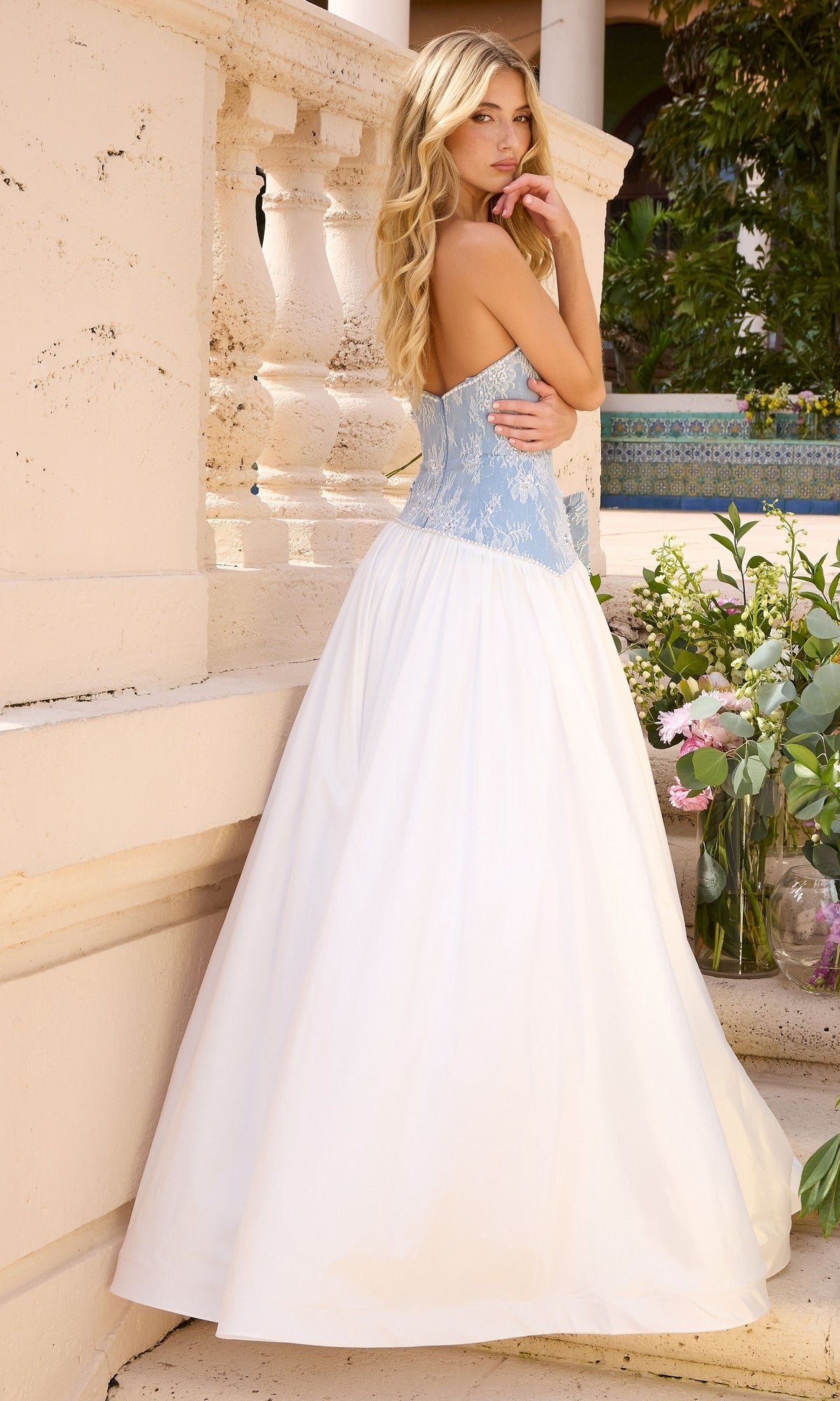 A woman wears a Long Prom Dress: Ava Presley 43127 featuring a light blue lace bodice and a voluminous white skirt.