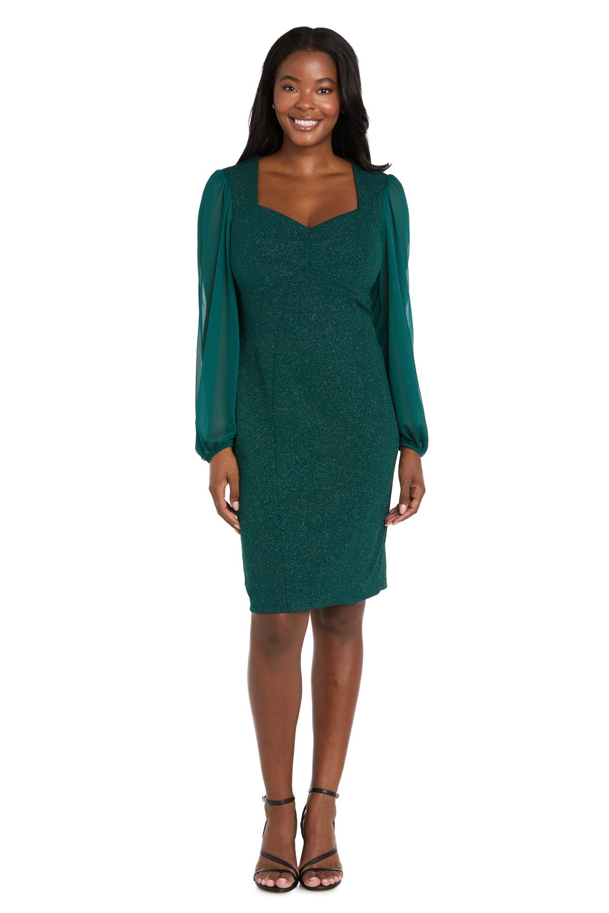 A woman stands and smiles against a white background, wearing the Knee Length Green Party Dress: R&M Richards 4331, featuring long sheer sleeves.