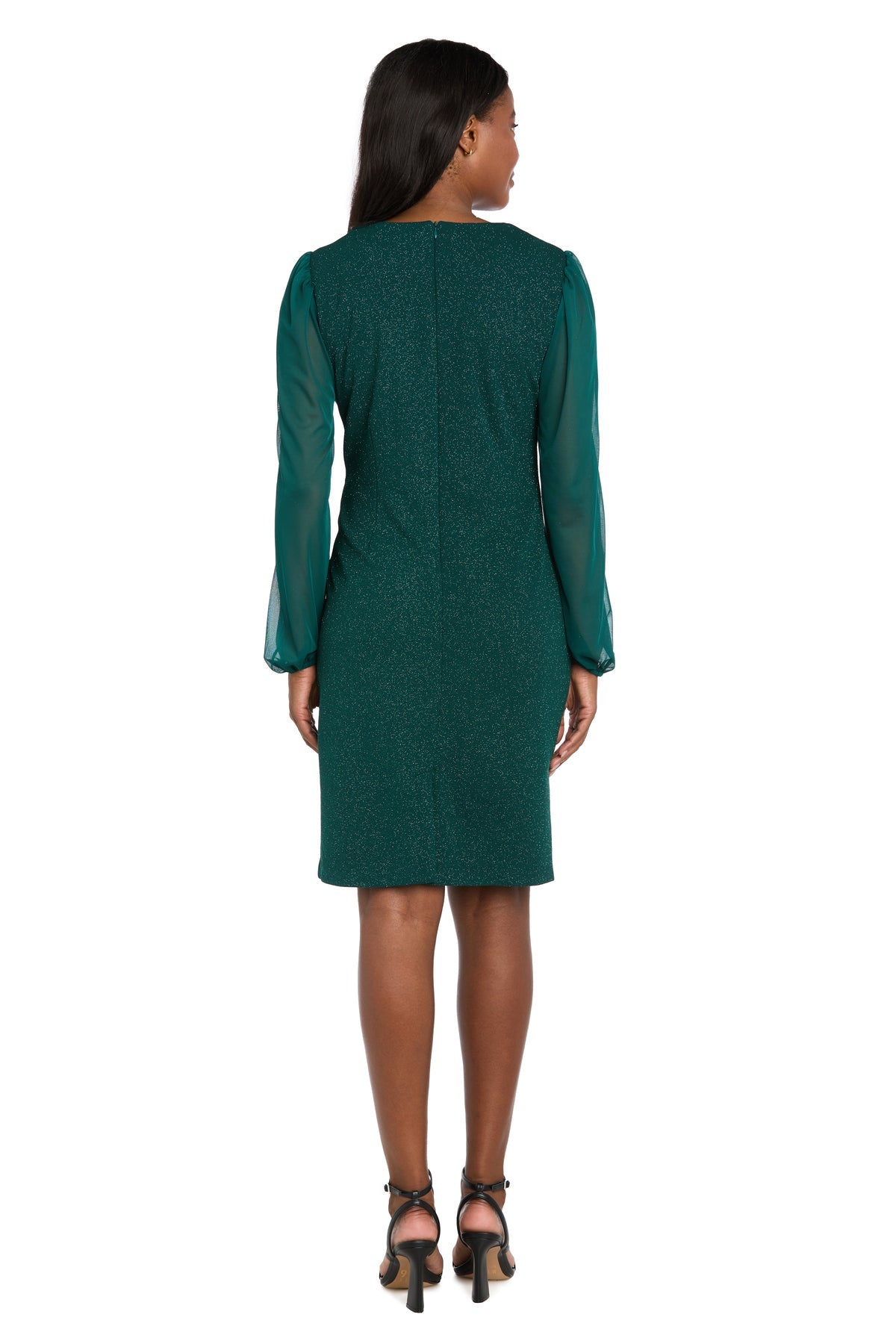 A woman stands facing away, wearing the R&M Richards 4331 knee-length green party dress with sheer long sleeves and black high-heeled sandals.