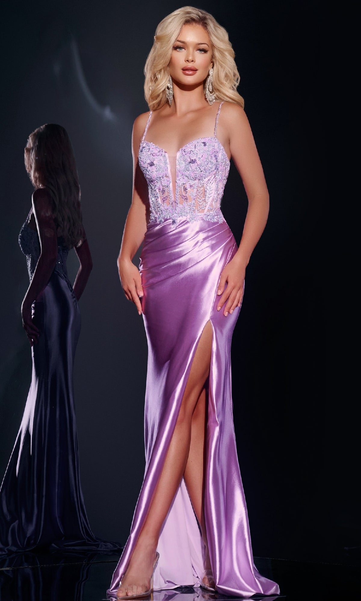 A woman poses in the Long Prom Dress: Jovani 43569, featuring a sleeveless design, lilac satin skirt with thigh-high slit, and a sheer embellished bodice; her reflection appears behind her.