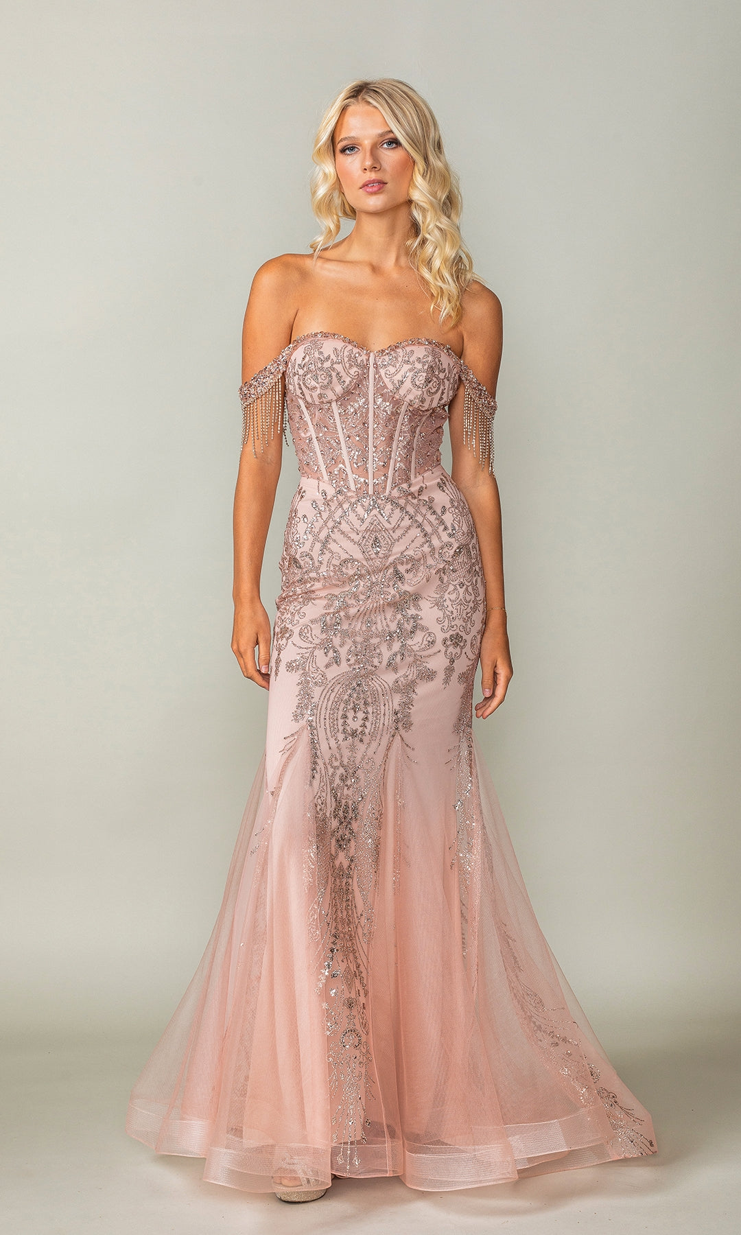 A woman wears the Fringe Long Glitter Prom Dress: Dancing Queen 4365 in blush pink, featuring an off-the-shoulder neckline, corset-style bodice, beaded details, and sheer panels, standing against a neutral background.