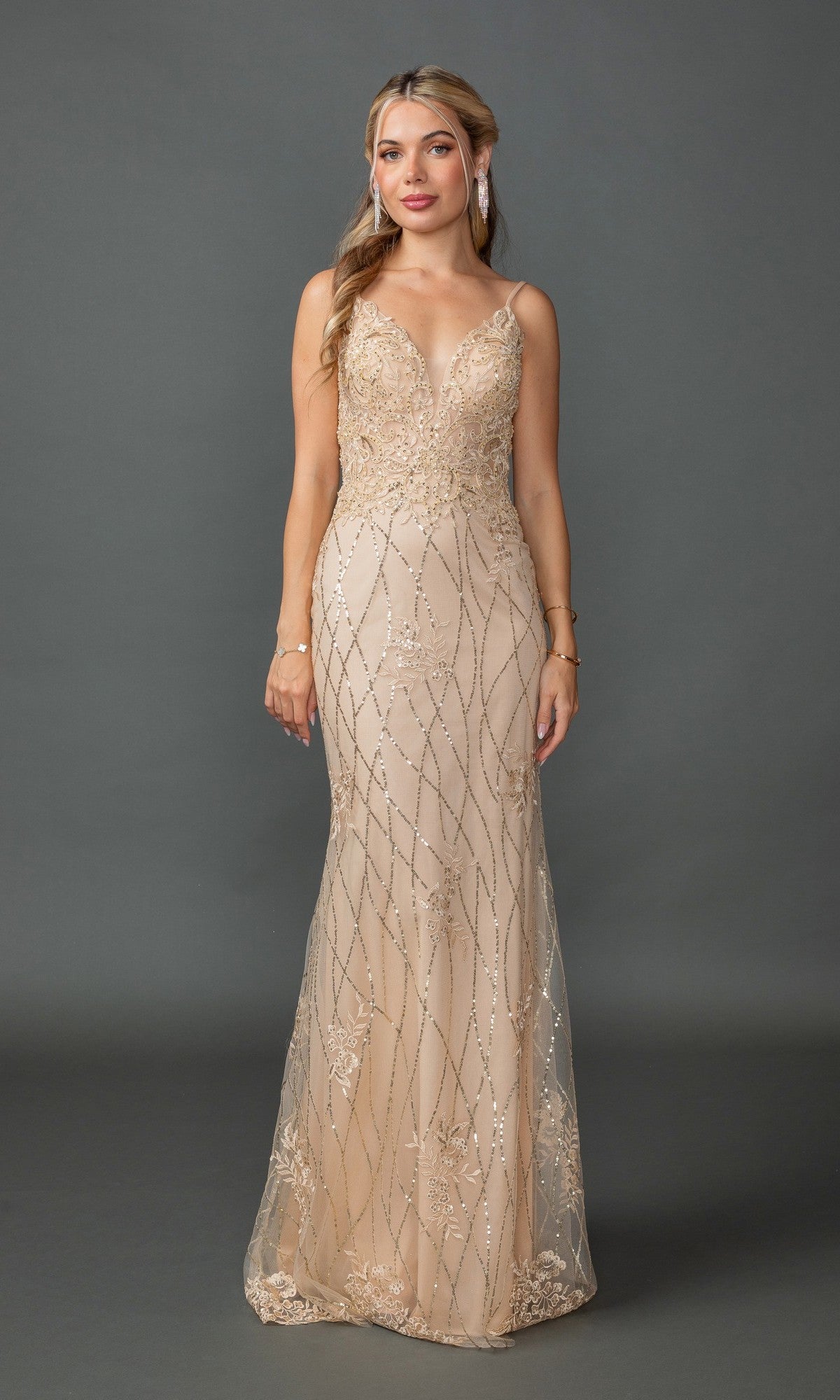 A woman poses against a gray background, wearing the Sequin-Print Long Prom Dress Dancing Queen 4371 in champagne—a sleeveless, floor-length gown with intricate beadwork and a fitted silhouette.