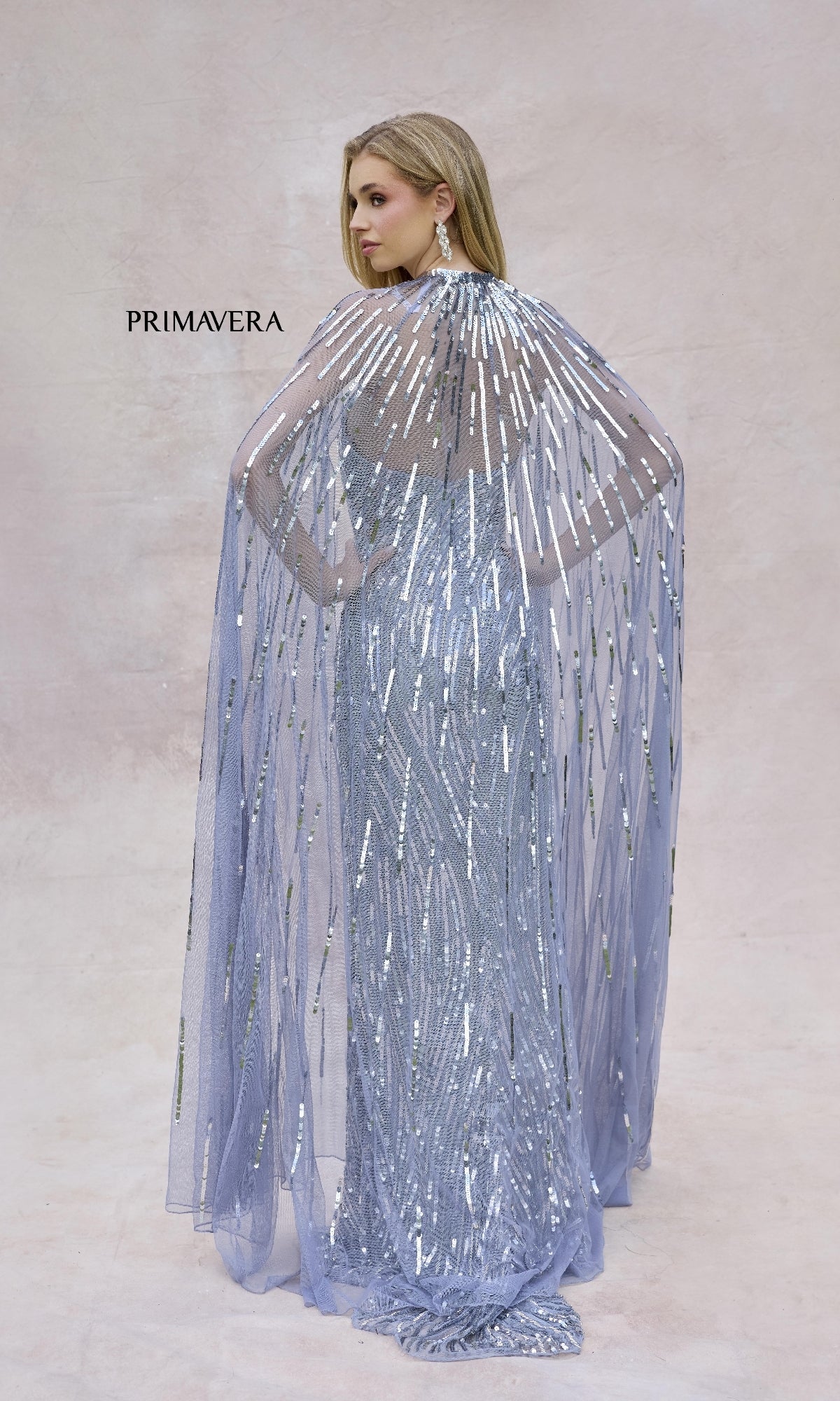 A woman faces away in the Primavera 4376 strapless sequined long prom dress with sheer matching cape, set against a neutral background.