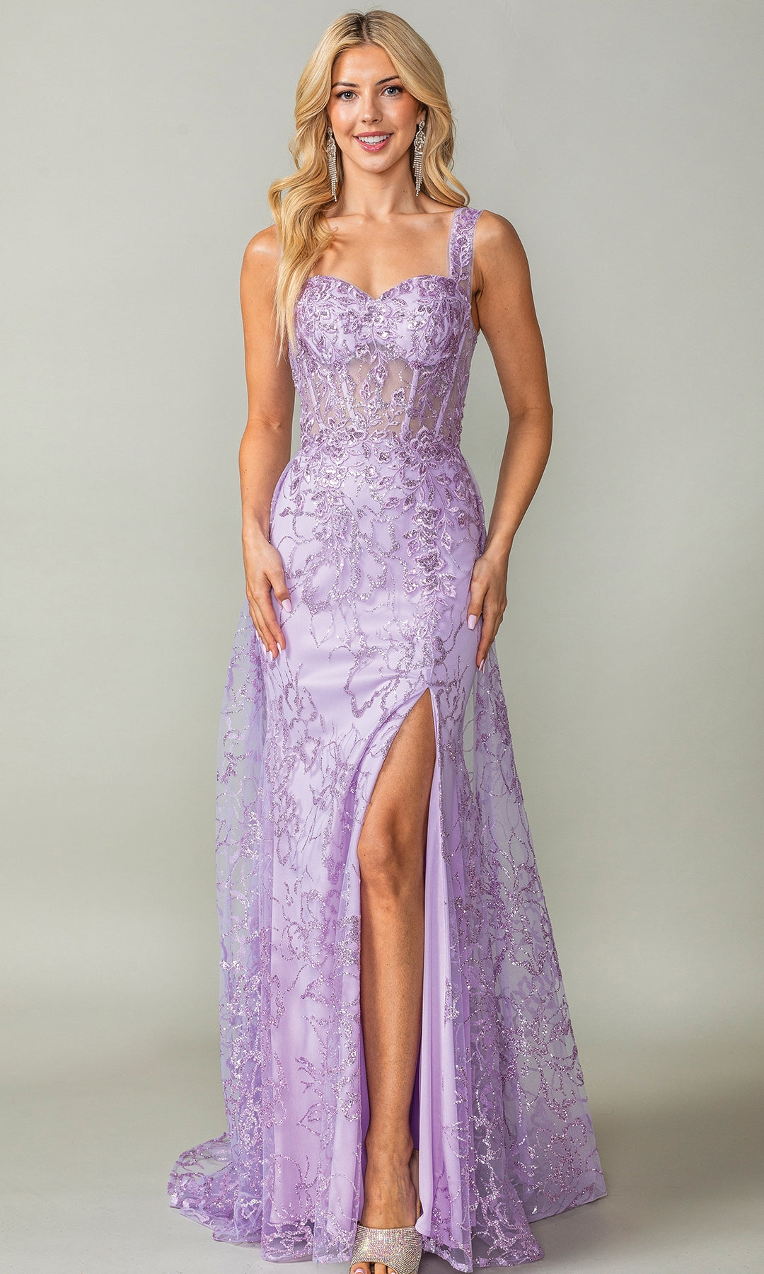 A woman wears the Glitter-Print Lace-Up Long Prom Dress 4379, a fitted, floor-length lavender gown with lace detailing, a sweetheart neckline, one shoulder strap, and a thigh-high slit, standing against a plain background.