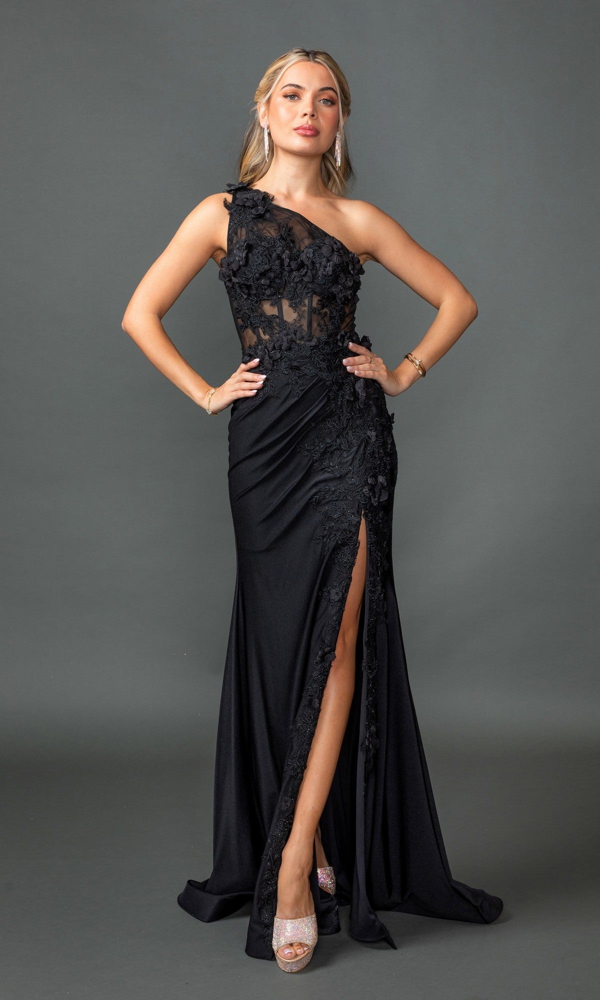 A woman poses against a plain gray background in the Dancing Queen 4381 one-shoulder long black prom dress, featuring a sheer corset-style bodice, lace detailing, and a thigh-high slit.