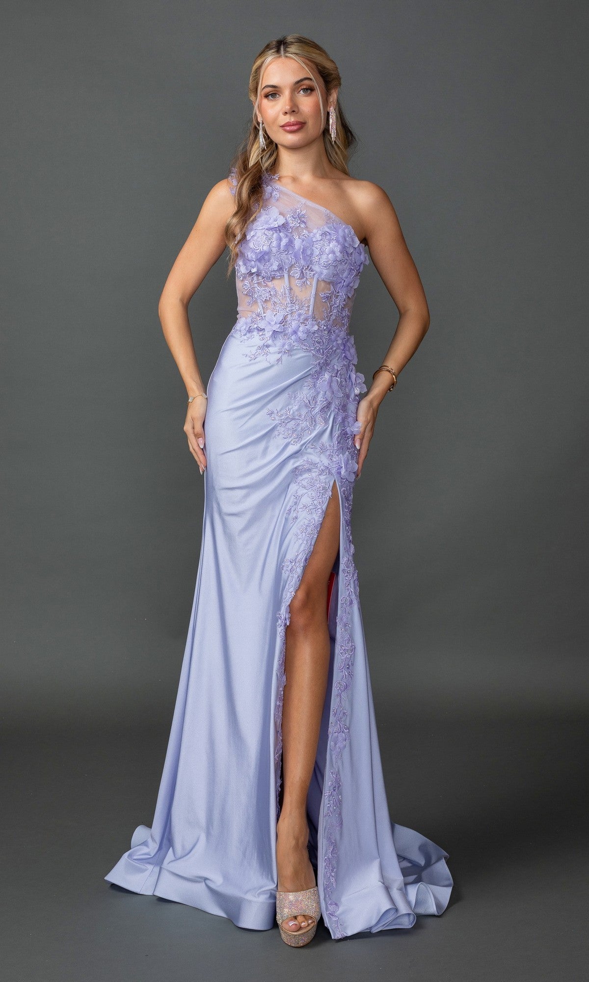 A woman in the Dancing Queen 4381, a light purple one-shoulder long prom dress with embroidered floral details, corset-style bodice, and thigh-high slit, poses elegantly against a plain gray background.
