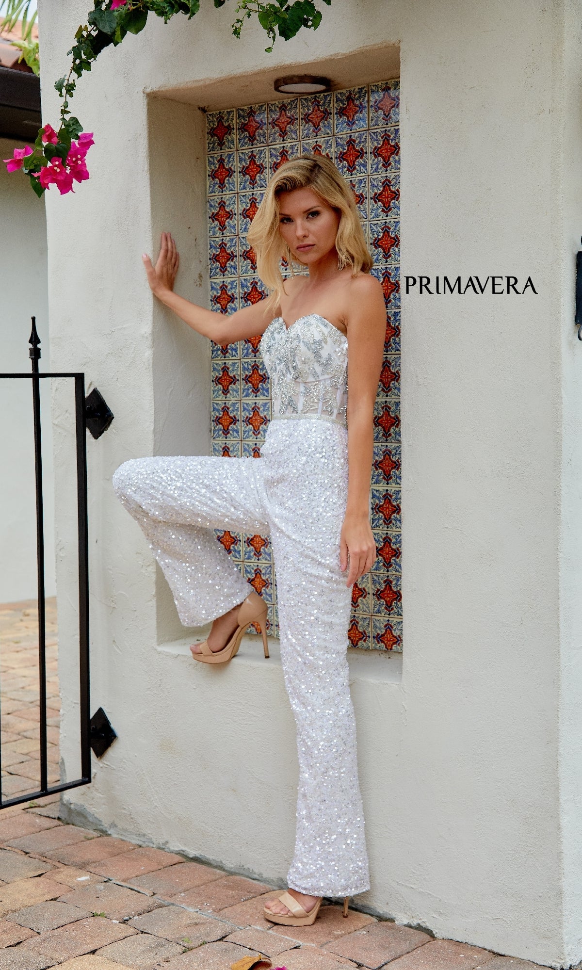 A woman poses in the Primavera 4383 Long Prom Jumpsuit, featuring sparkling sequins, against a tiled alcove with
