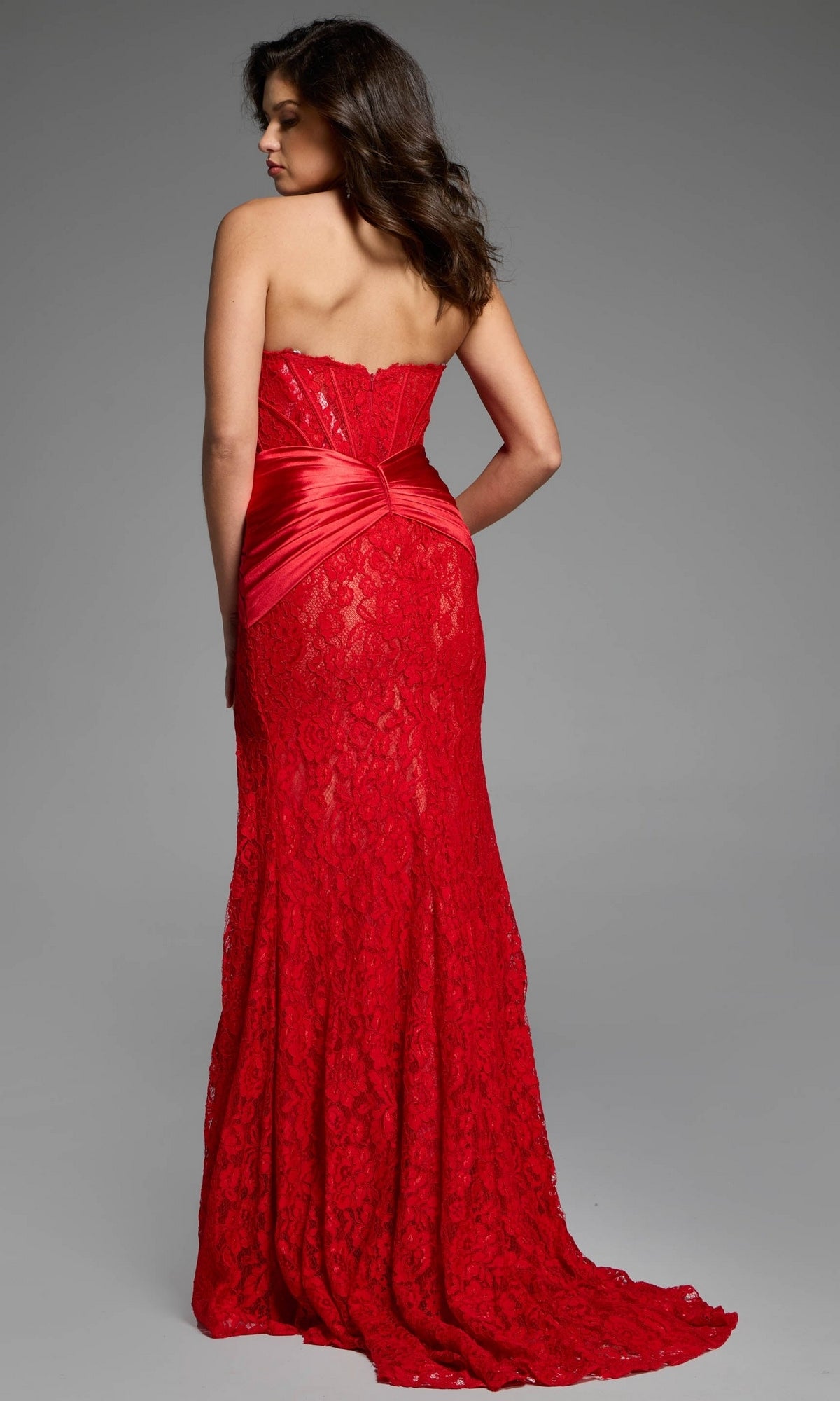 A woman wearing a Strapless Sweetheart Prom Gown: Jovani 43859, a floor-length red strapless lace dress with a cinched satin waist.