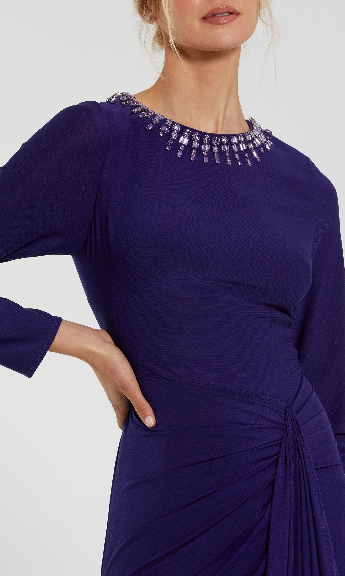 A woman models the Mac Duggal 44069, a modest long-sleeve formal dress in dark purple, featuring a ruched waist and a bead-embellished neckline for an elegant evening look.