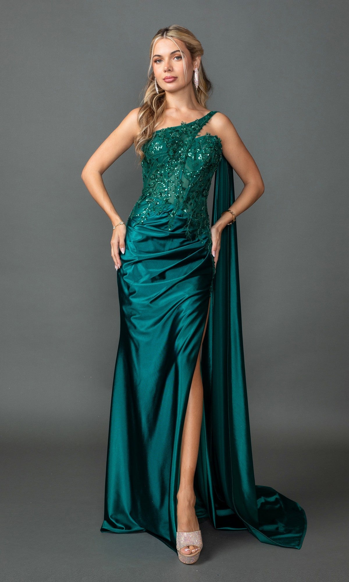 A woman poses against a plain gray background in the Dancing Queen 4441 one-shoulder long prom dress in hunter green, featuring satin fabric, a beaded-lace bodice, thigh-high slit, and draped sash.