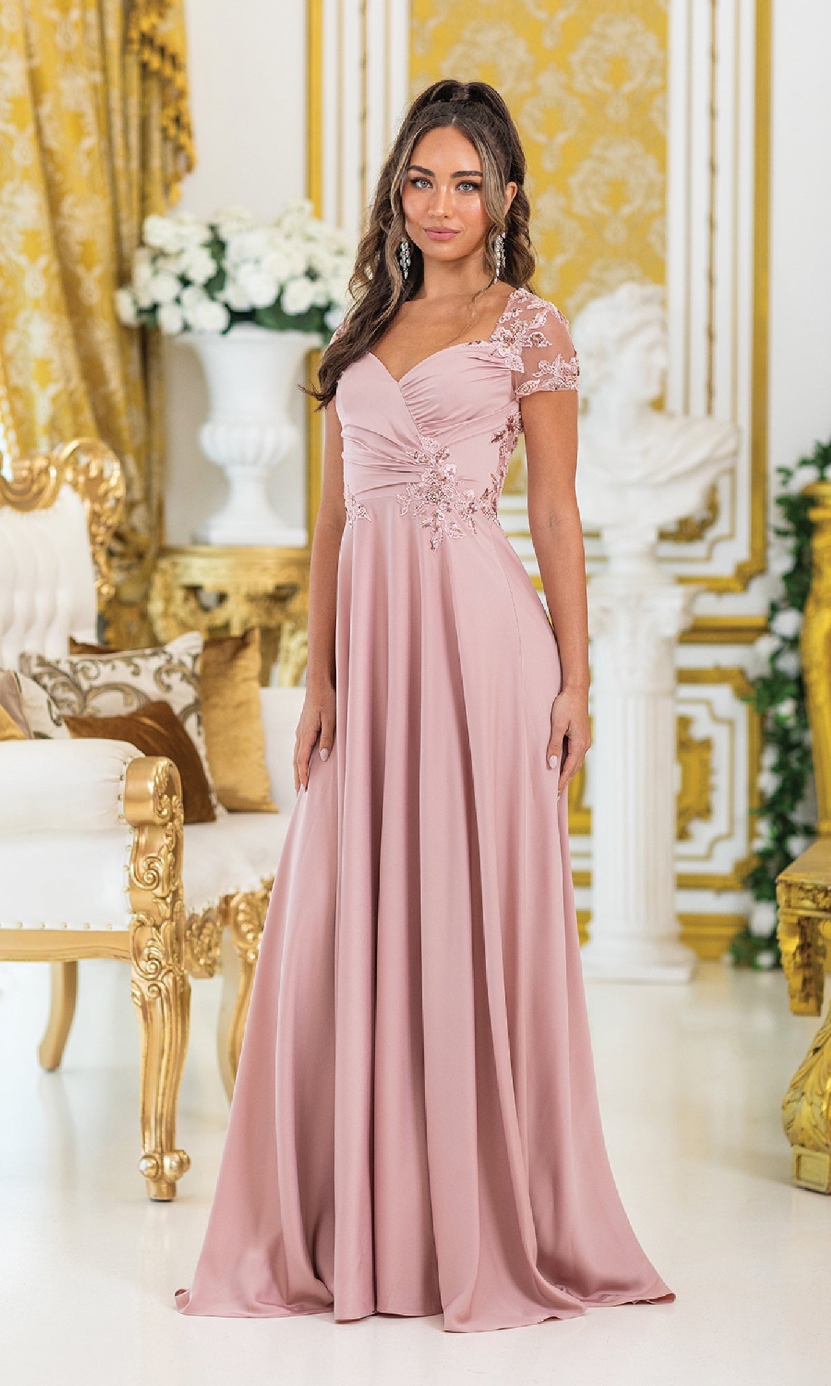 A woman in the Dancing Queen 4499 short-sleeve long prom dress stands in an ornately decorated room with gold and white furnishings.