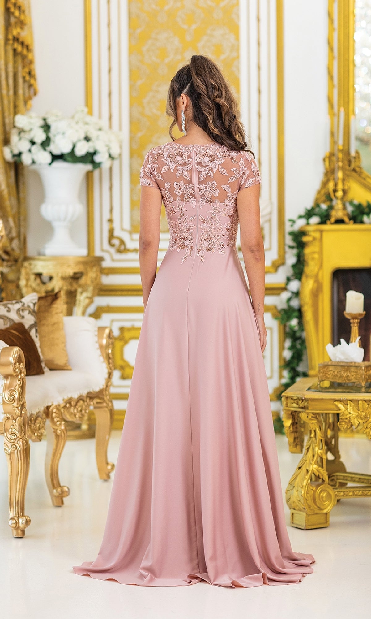 A woman stands with her back to the camera in an ornate, gold-accented room, wearing the Dancing Queen 4499: a floor-length, dusty pink a-line prom dress with lace detailing and short sleeves.
