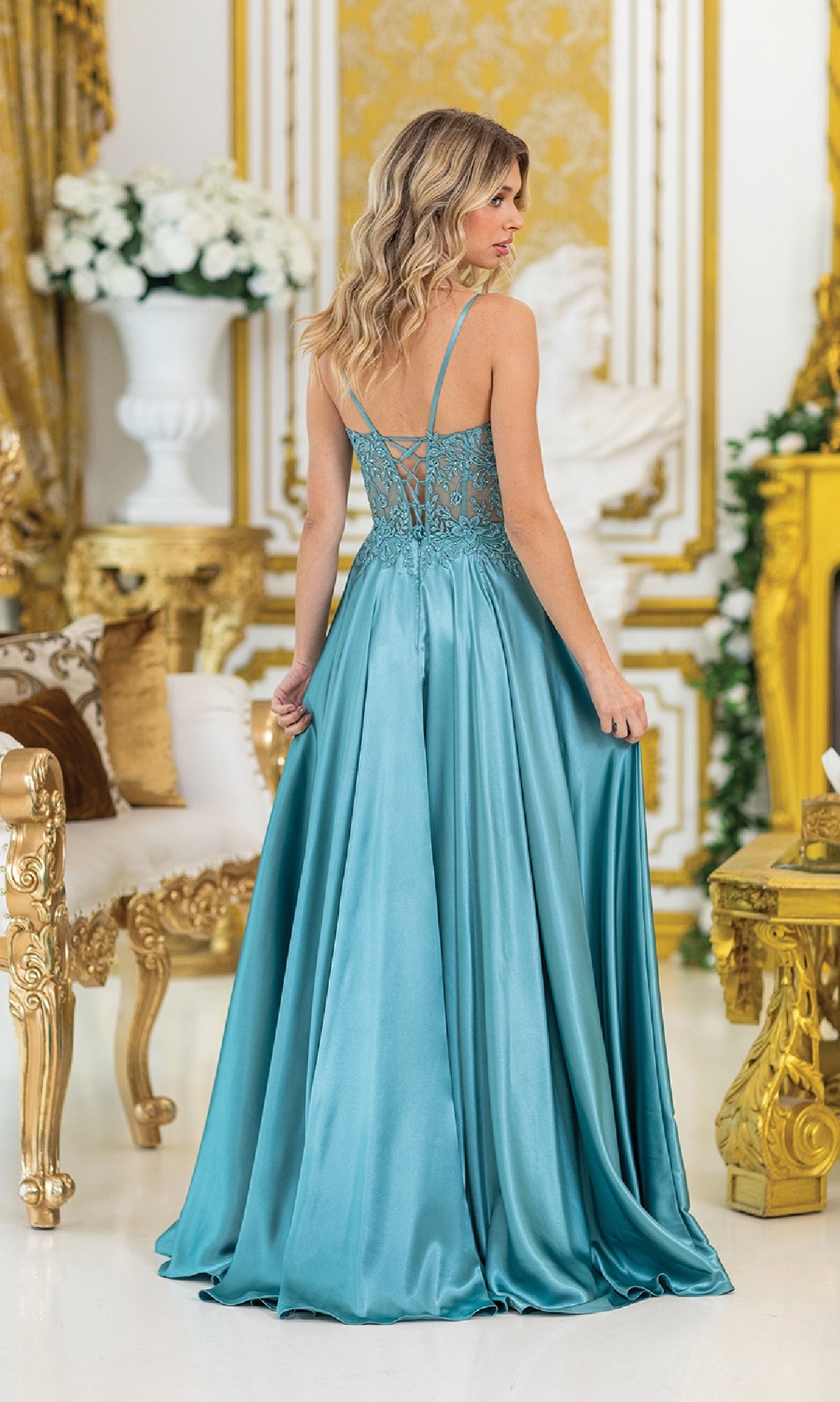 A woman in the Sheer-Waist Long Prom Dress: Dancing Queen 4520, a teal satin gown with a sweetheart neckline and lace details, stands with her back to the camera in an ornate room accented with gold.