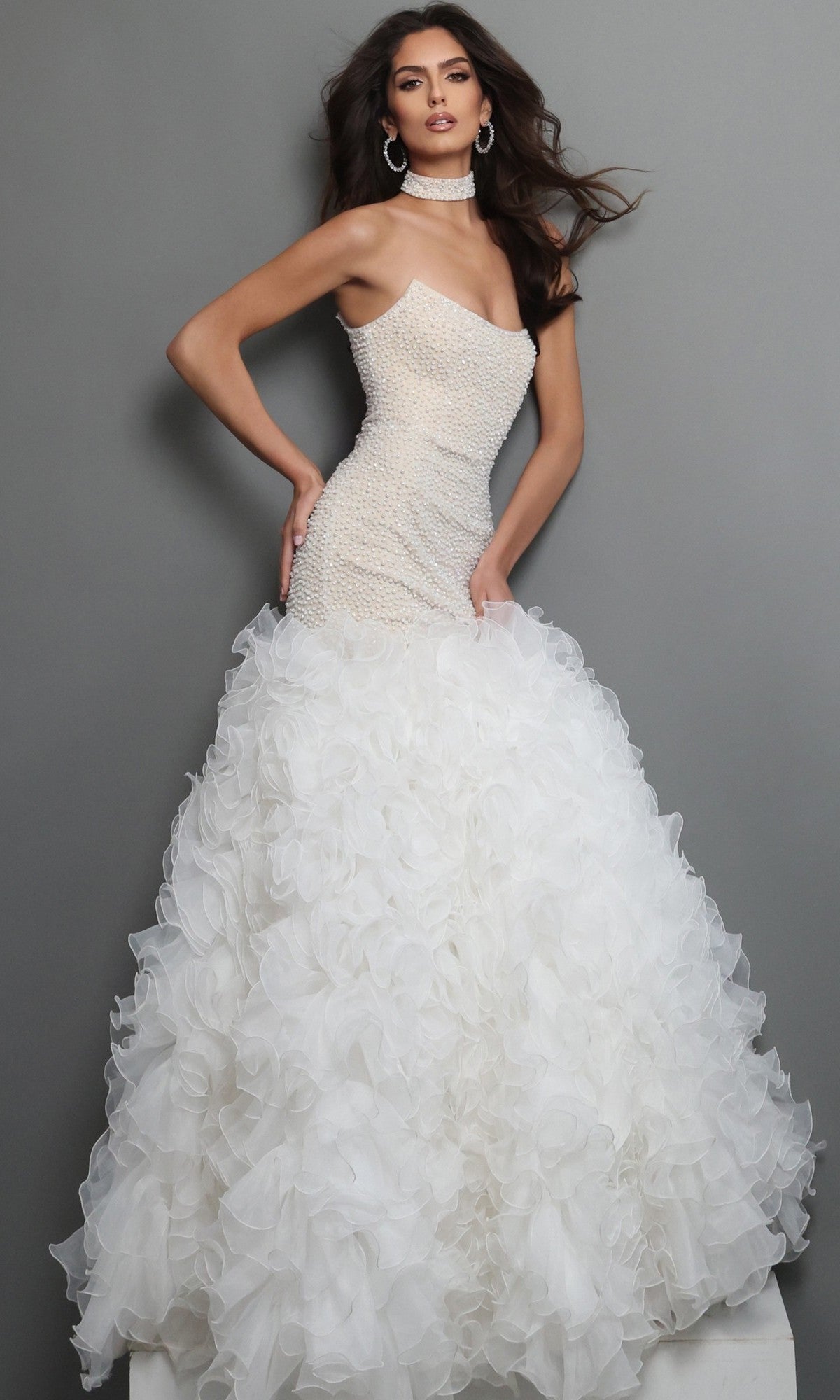 A woman wearing the Jovani 45339 long formal dress in off-white/nude, featuring a strapless fitted beaded bodice and a voluminous ruffled skirt, poses against a plain gray background.