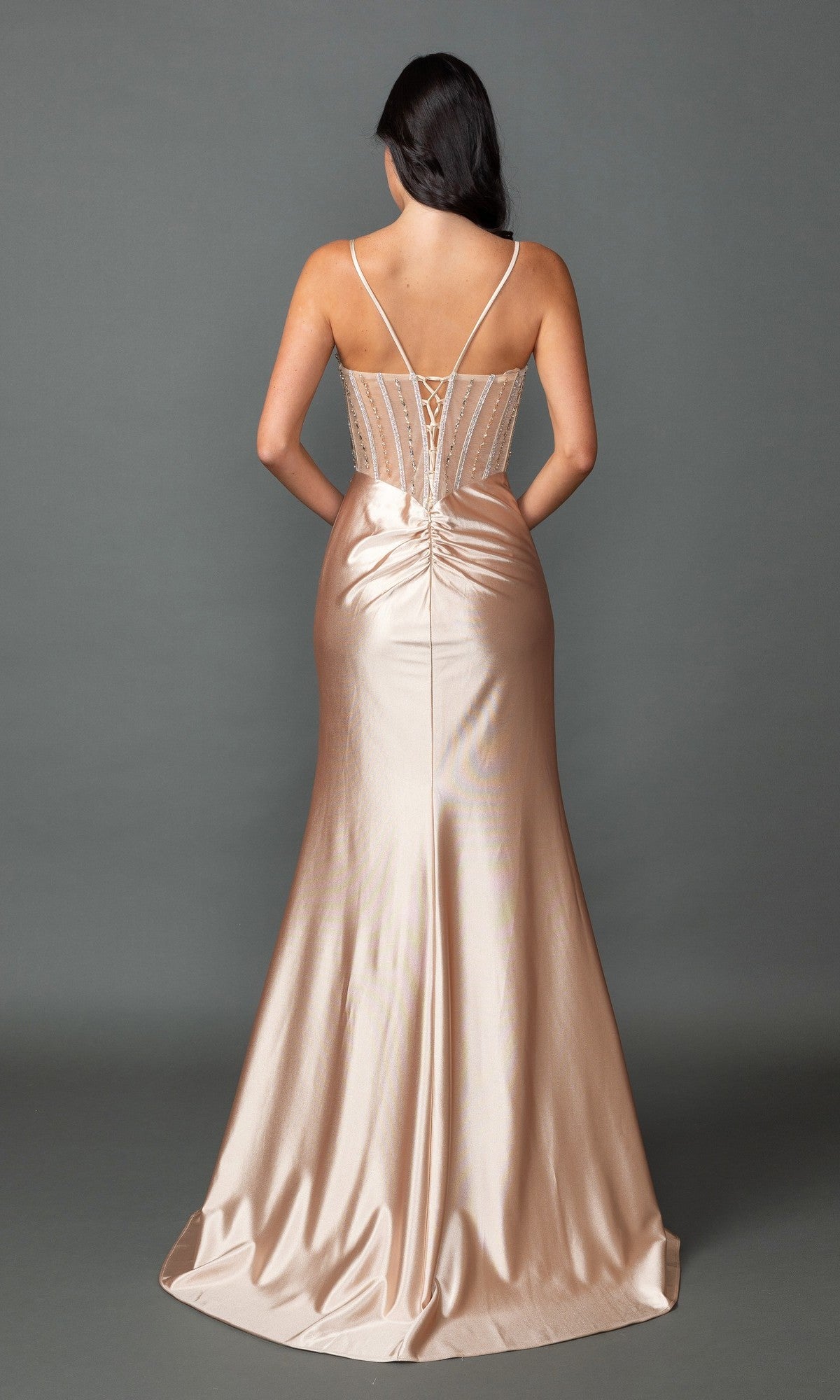 A woman faces away, wearing the Dancing Queen 4561 long prom dress in champagne. The shiny gown features thin straps and a lace-up corset back, with an elegant floor-length silhouette.