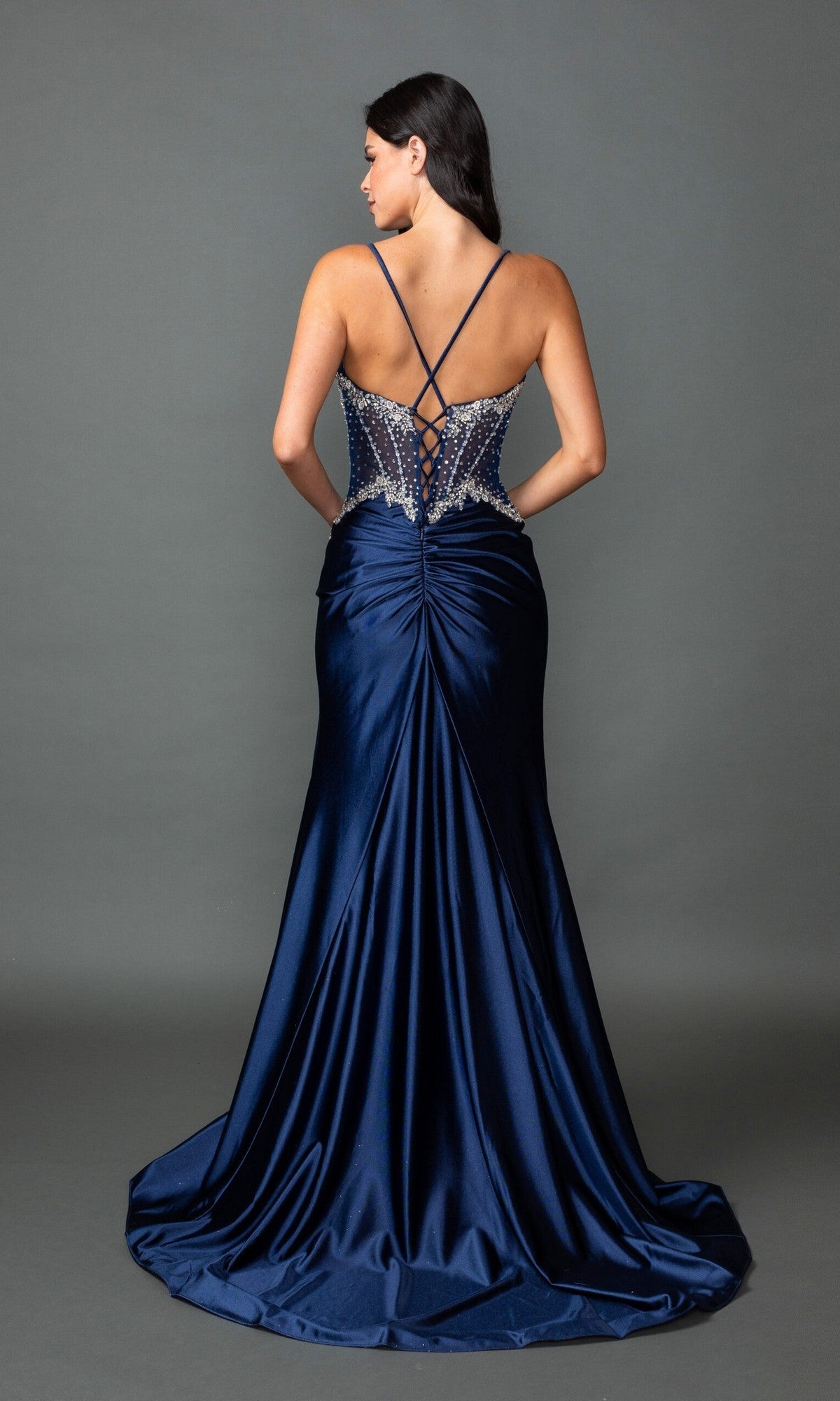A woman models the Dancing Queen 4579 long prom dress in navy blue, featuring beaded jeweled accents and a lace-up back, standing before a plain gray background.
