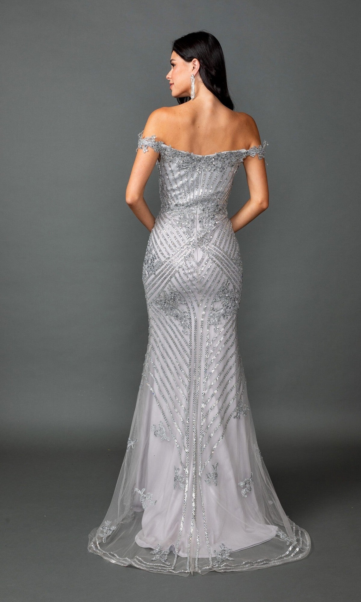 A woman wearing the Long Prom Dress: Dancing Queen 4600, a silver off-the-shoulder gown with bead embellishments, stands against a plain gray background facing away from the camera.