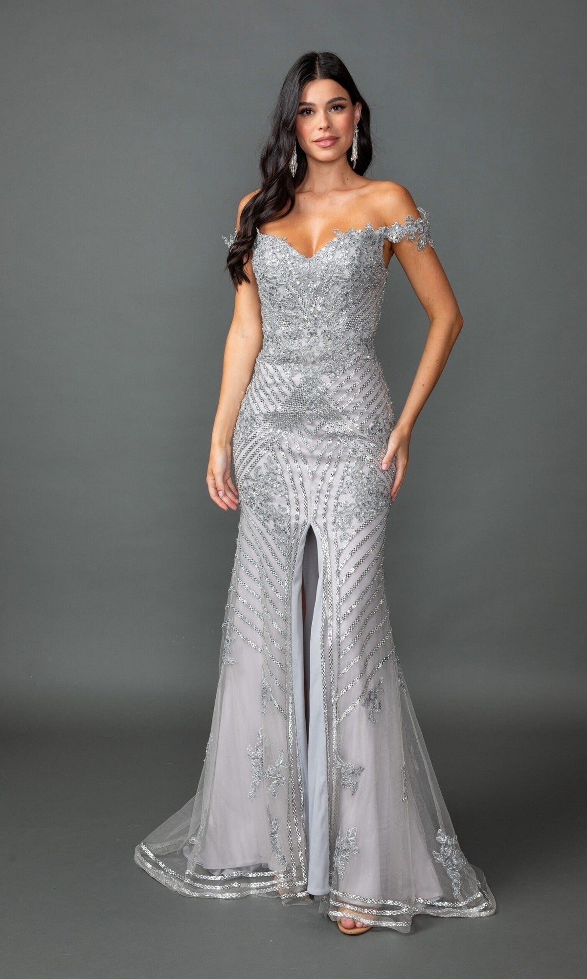 A woman wearing the Dancing Queen 4600 long prom dress in silver, designed with an off-the-shoulder neckline, beaded embellishments, and a front slit, stands against a plain gray background.