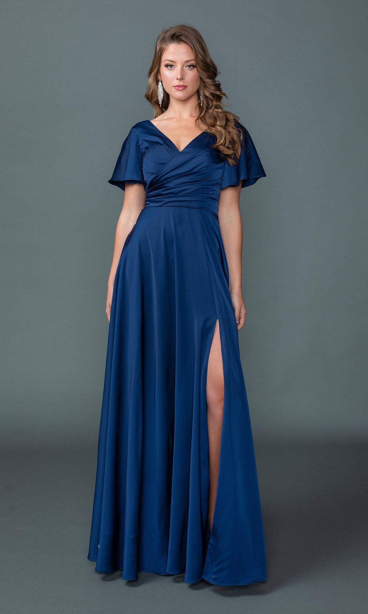 A woman wears the Dancing Queen 4602 long formal navy dress, featuring short flutter sleeves, a v-neckline, ruched bodice, and a thigh-high slit, standing against a plain gray background.