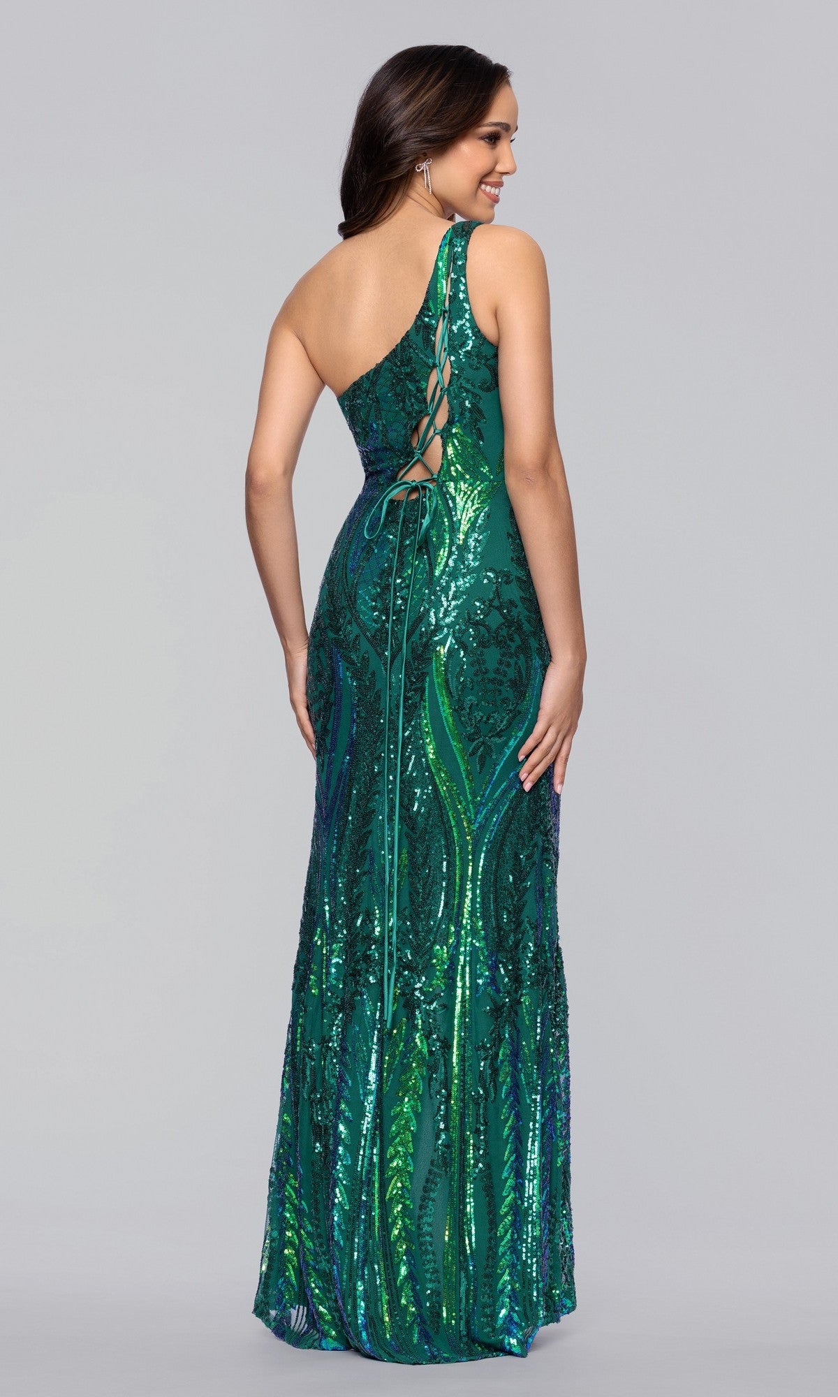 Woman in the Long Sequin-Print Prom Dress by Blondie Nites 4610BN, a floor-length emerald gown with one shoulder strap and lace-up back, stands facing away from the camera.