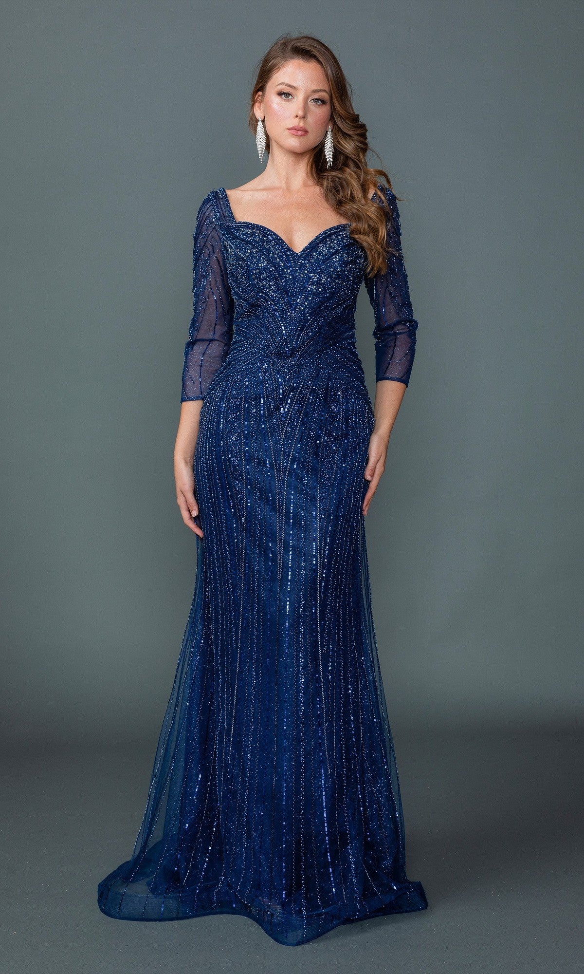 A woman stands against a plain gray background wearing the navy Long Formal Dress: Dancing Queen 4611, a floor-length gown with embellishments and three-quarter sleeves.