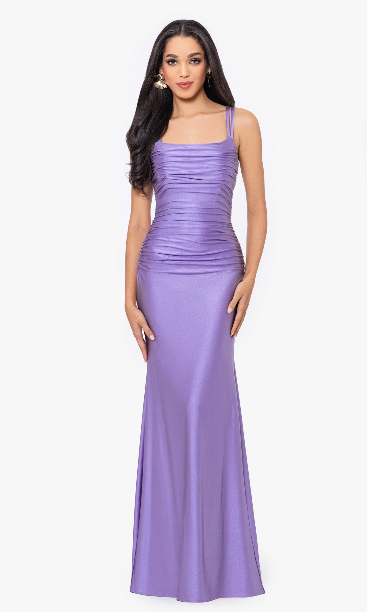 A woman stands facing forward in the Blondie Nites Long Lavender Prom Dress 4639BN, a junior-size evening gown featuring a floor-length silhouette and ruched bodice detailing.