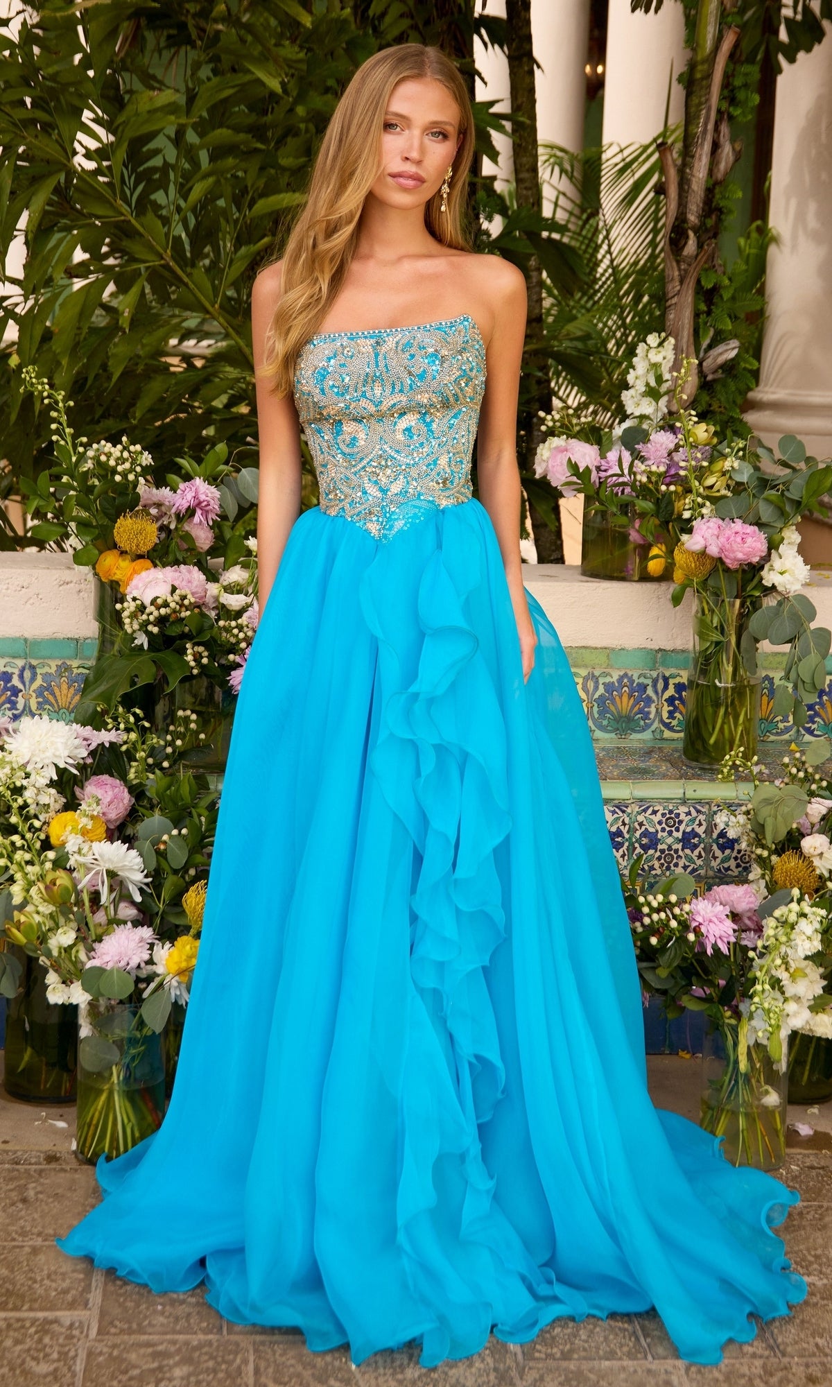 A model wears a turquoise gold Ava Presley 47420 strapless gown with a gold-embroidered bodice and a full, floor-length skirt featuring a ruffled side detail.