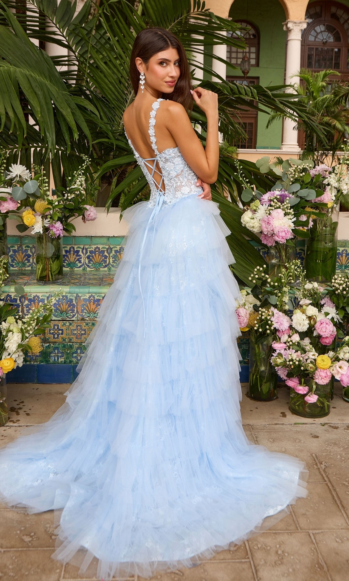 A woman wears an Ava Presley 47463 floor-length prom dress featuring a lace bodice with 3D flowers, a corset back, and a layered tulle skirt.