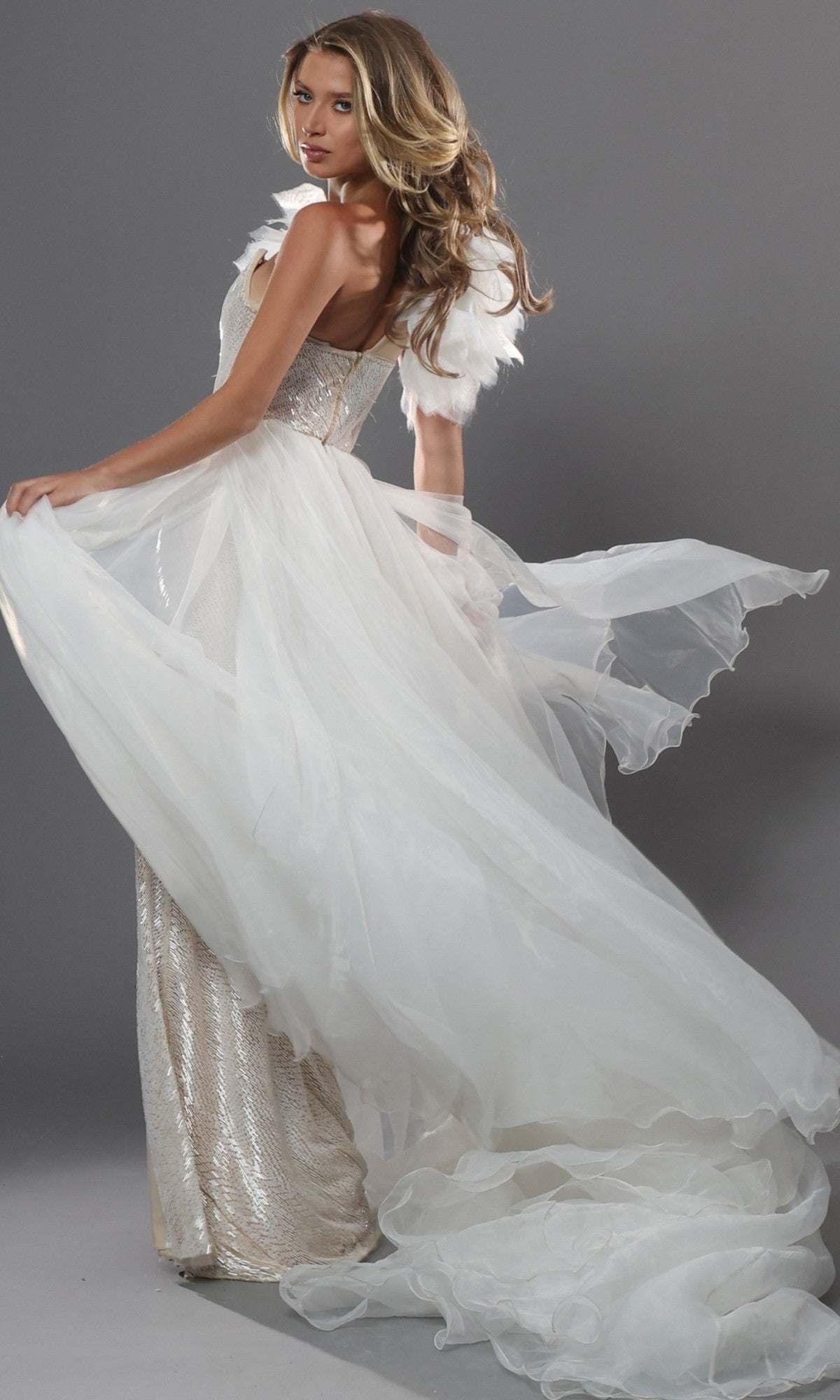 A woman poses against a gray background wearing the Jovani 47895 long formal dress, featuring a flowing off-white design with a sheer train and feathered shoulder detail.