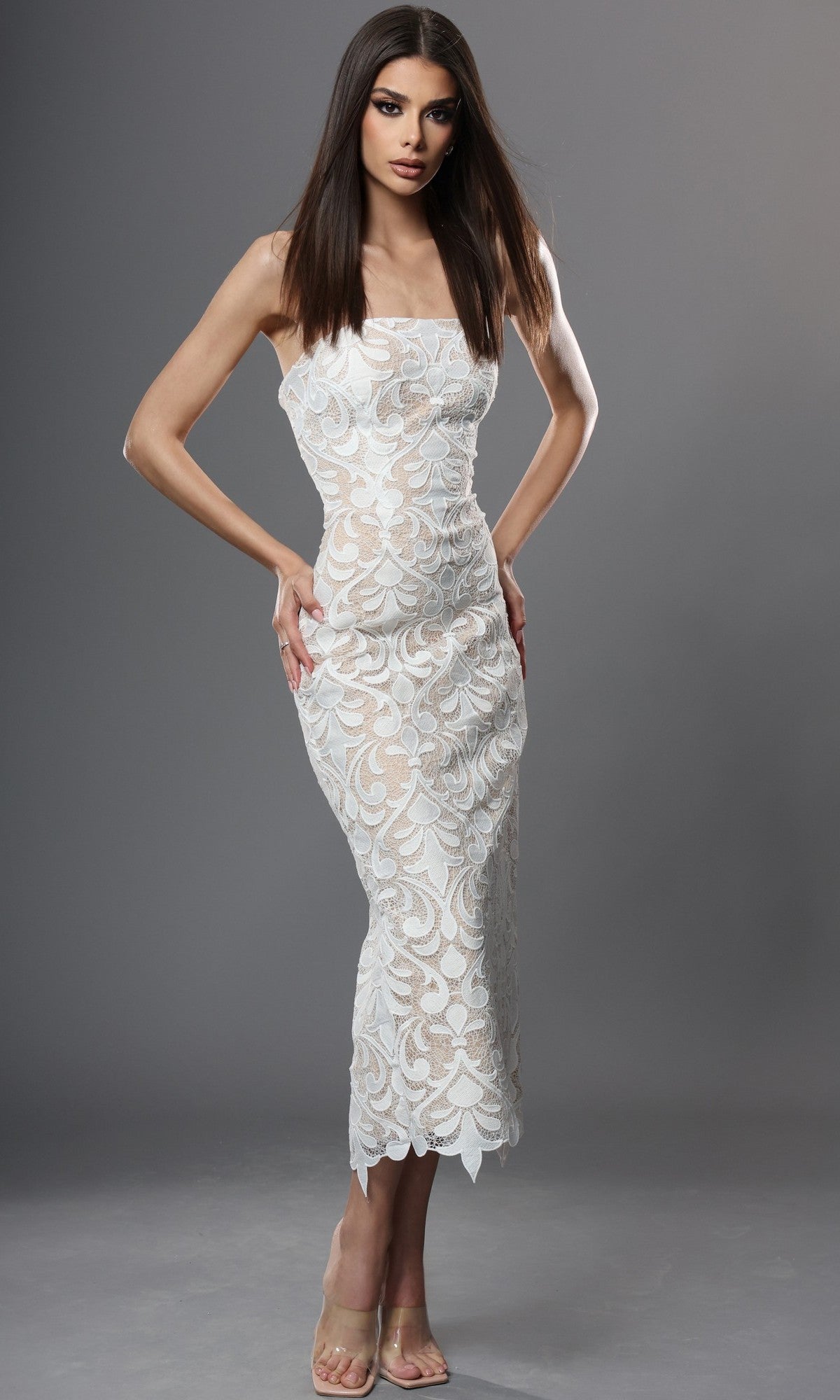 An elegant woman poses against a plain gray background in the Midi Semi-Formal Dress: Jovani 48461, a stunning off white/nude strapless lace dress featuring a form-fitting silhouette with a sheer floral pattern—making it the perfect choice for any special occasion.