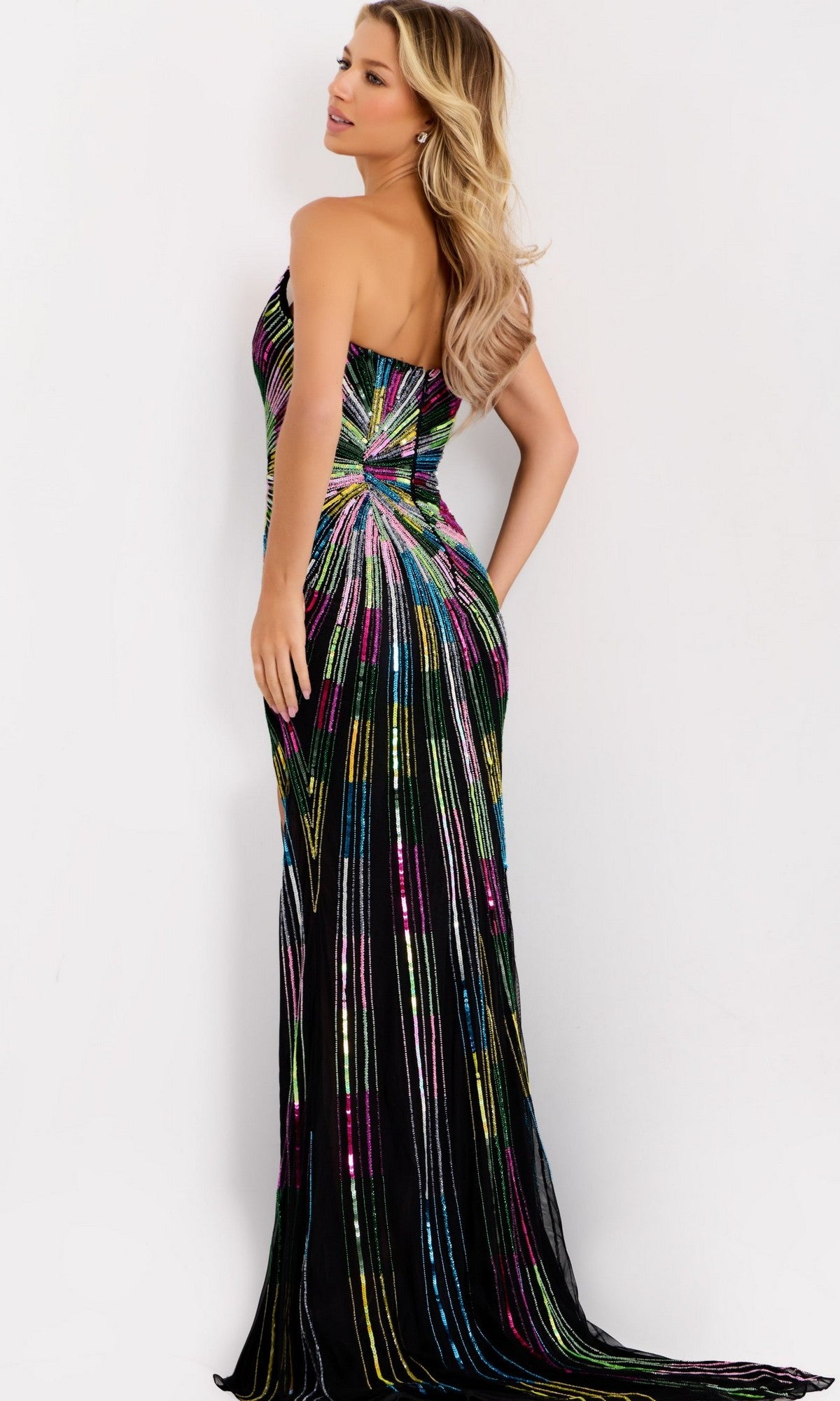 A woman models the Jovani 48564 long prom dress, featuring colorful vertical sequin stripes, standing with her back to the camera, one hand on her hip and her long blonde hair draped over her shoulder.