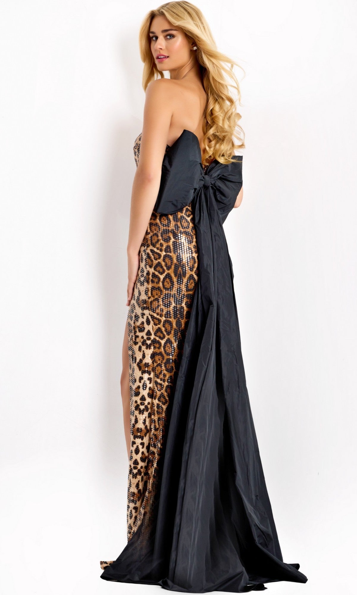 A woman wearing the Jovani 48651 long prom dress, featuring a strapless leopard-print sequin design with a sweetheart neckline, high front slit, and a large black bow with an elegant long black train at the back.